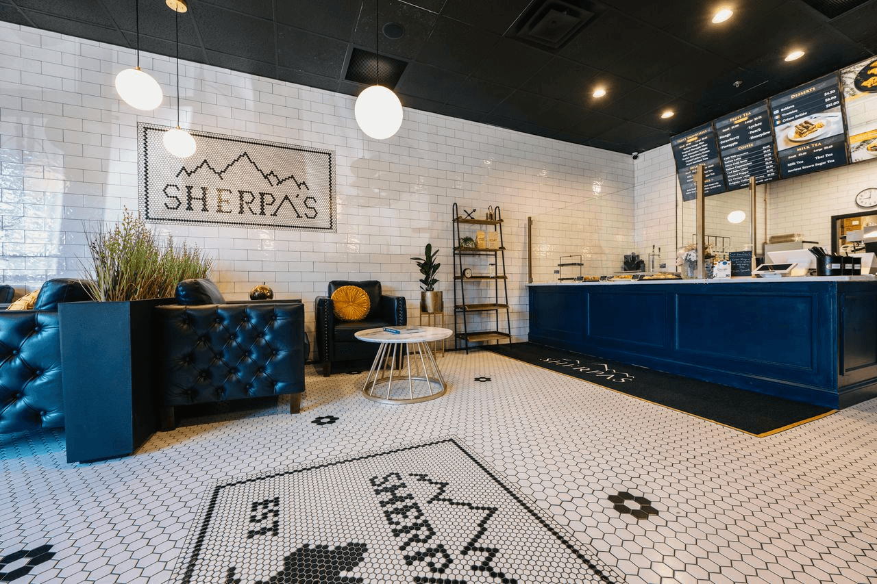 Interior of Café Sherpa's in Brookfield, WI featuring custom mosaic tile floors, tufted leather seating, and a navy blue service counter. A curated, inviting café space worth visiting in person.