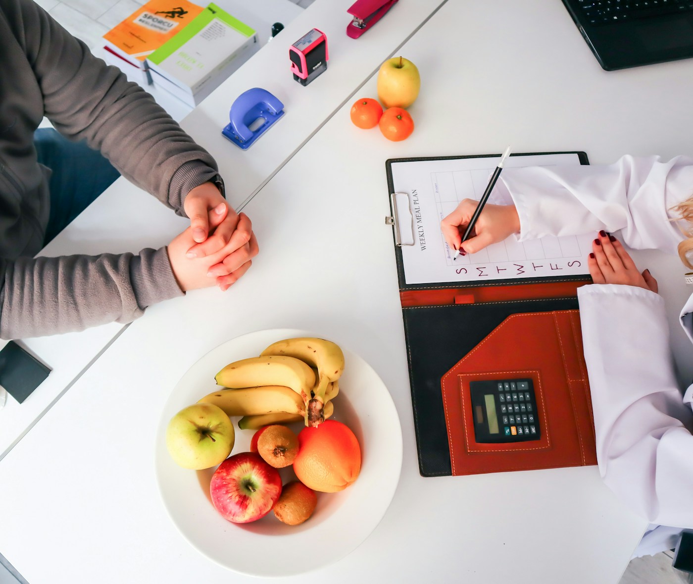 A dietitian writing notes across a table from a client, with a bowl of fresh fruit between them