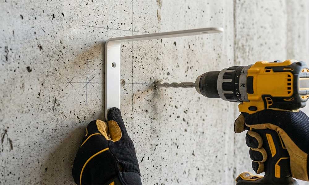 Handwerker bohrt mit Akku-Schlagbohrmaschine Befestigungsloch in Betonwand für Winkelkonsole