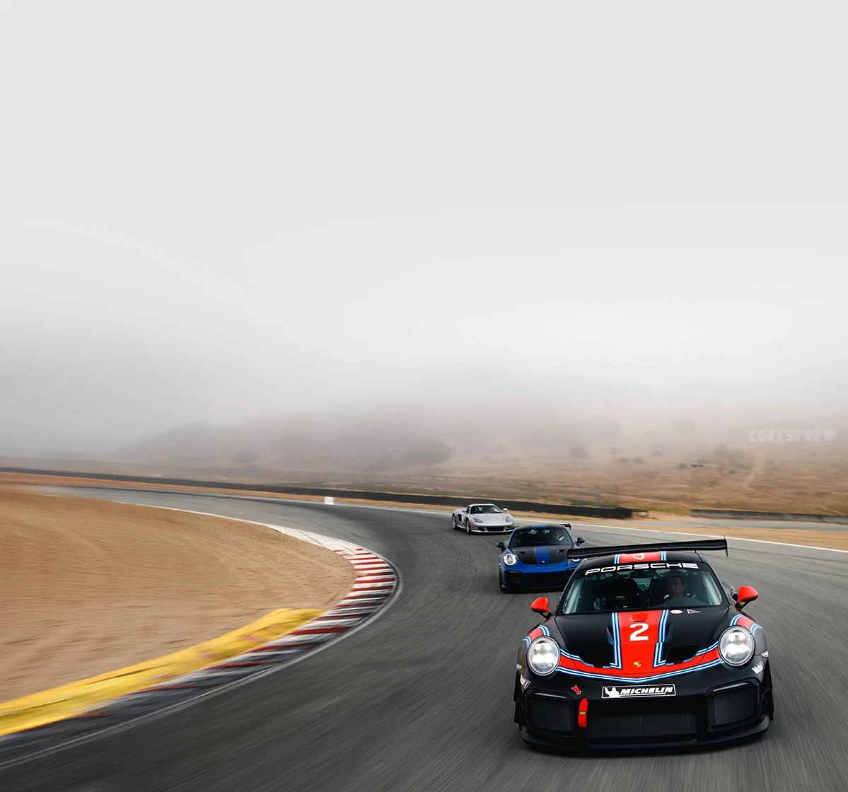 Three Porsche race cars rounding a turn on the track.