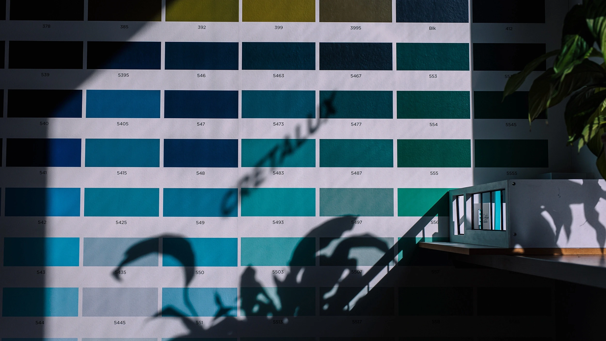 A close-up view of building windows reflecting light and greenery in the foreground, creating a pattern of shadows.