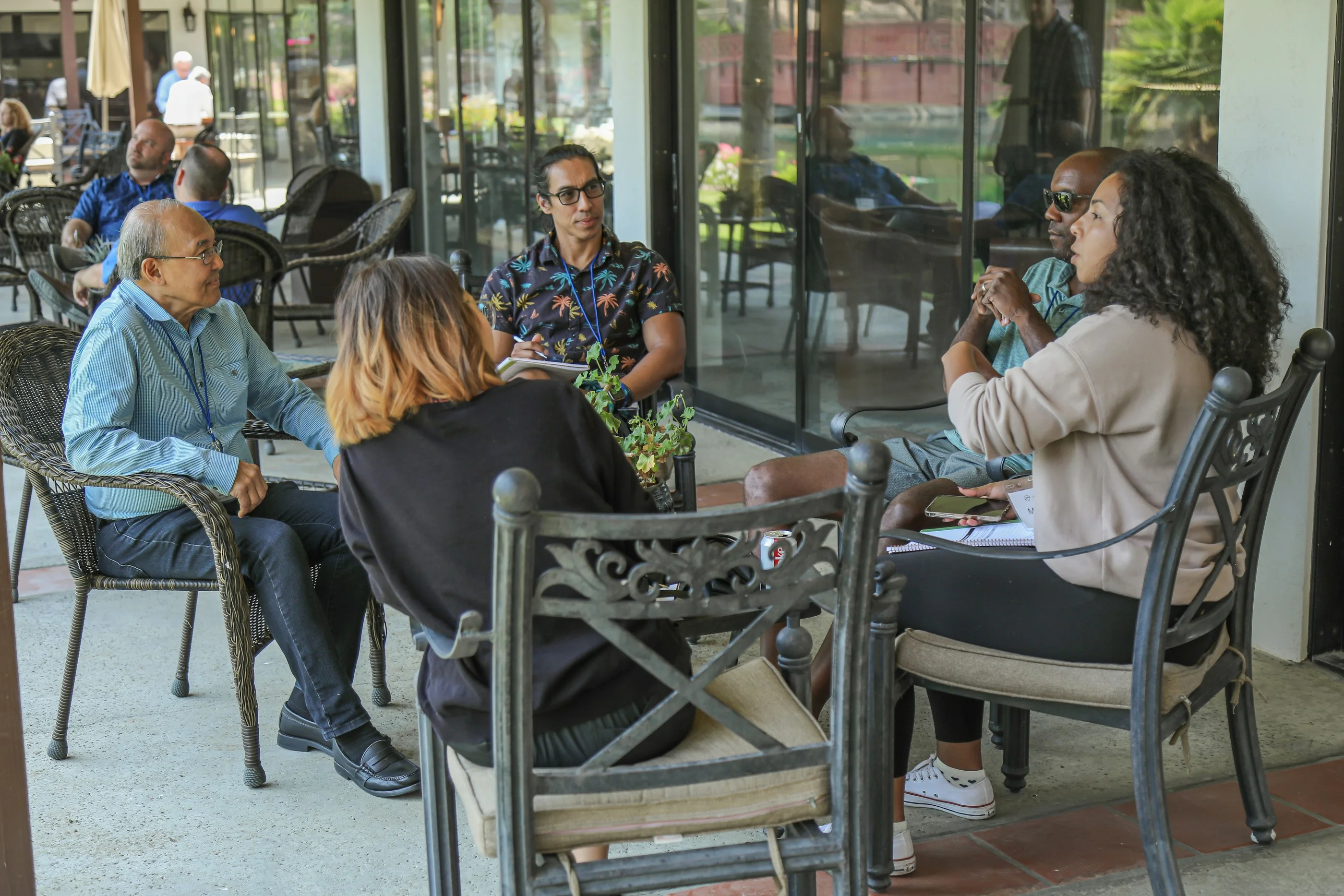 A small group talking in a circle of chairs on a shaded patio