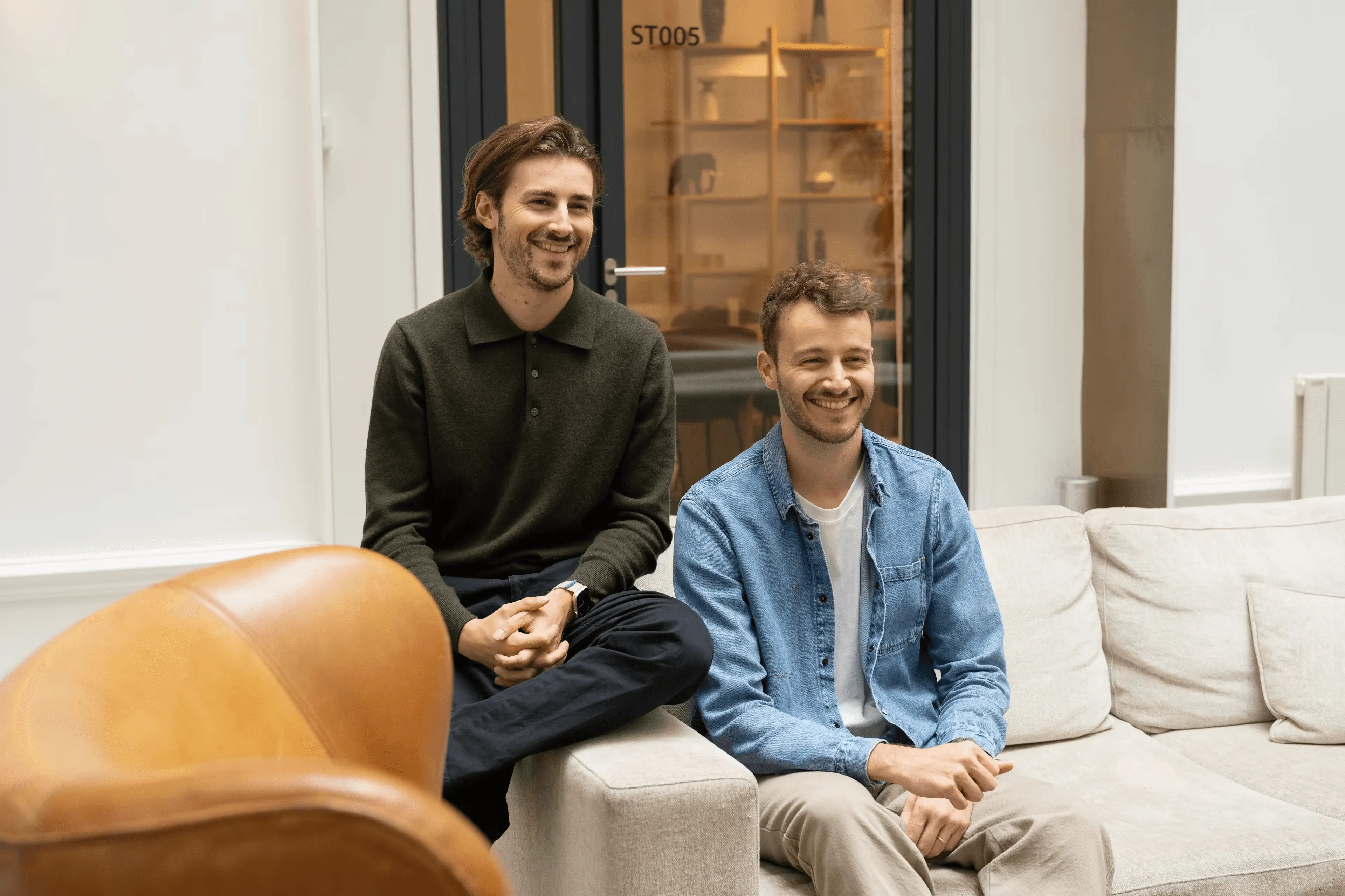 A smiling woman is standing and applauding during a friendly team meeting, surrounded by attentive colleagues in a bright space.
