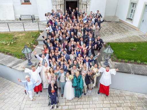Hochzeitsgesellschaft als Gruppenfoto vor Kirche aus erhöhter Perspektive Drone
