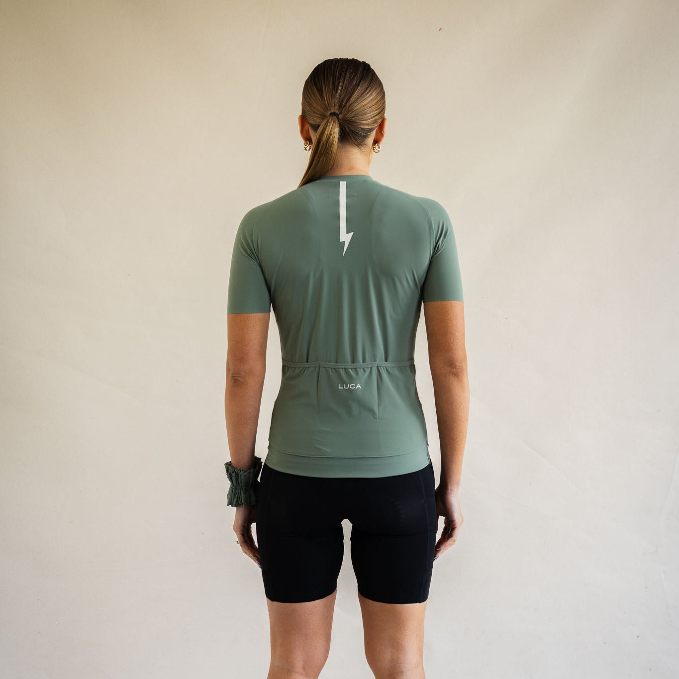 Cyclist wearing LUCA Soleil jersey in matcha, back view with rear pocket detail