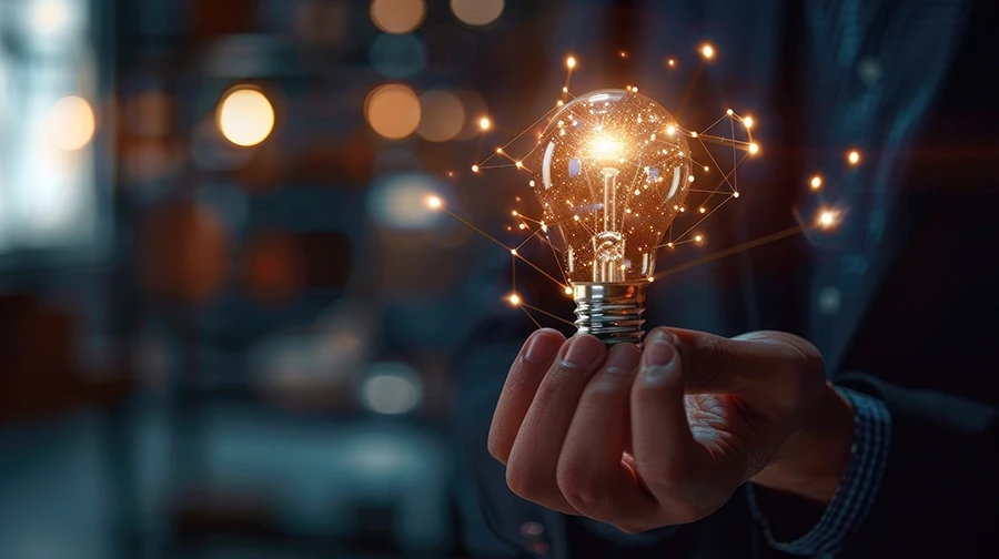 Eine Person hält eine leuchtende Glühbirne, die Innovation symbolisiert, während digitale Netzwerkverbindungen von ihr ausgehen, vor einem unscharfen Hintergrund.