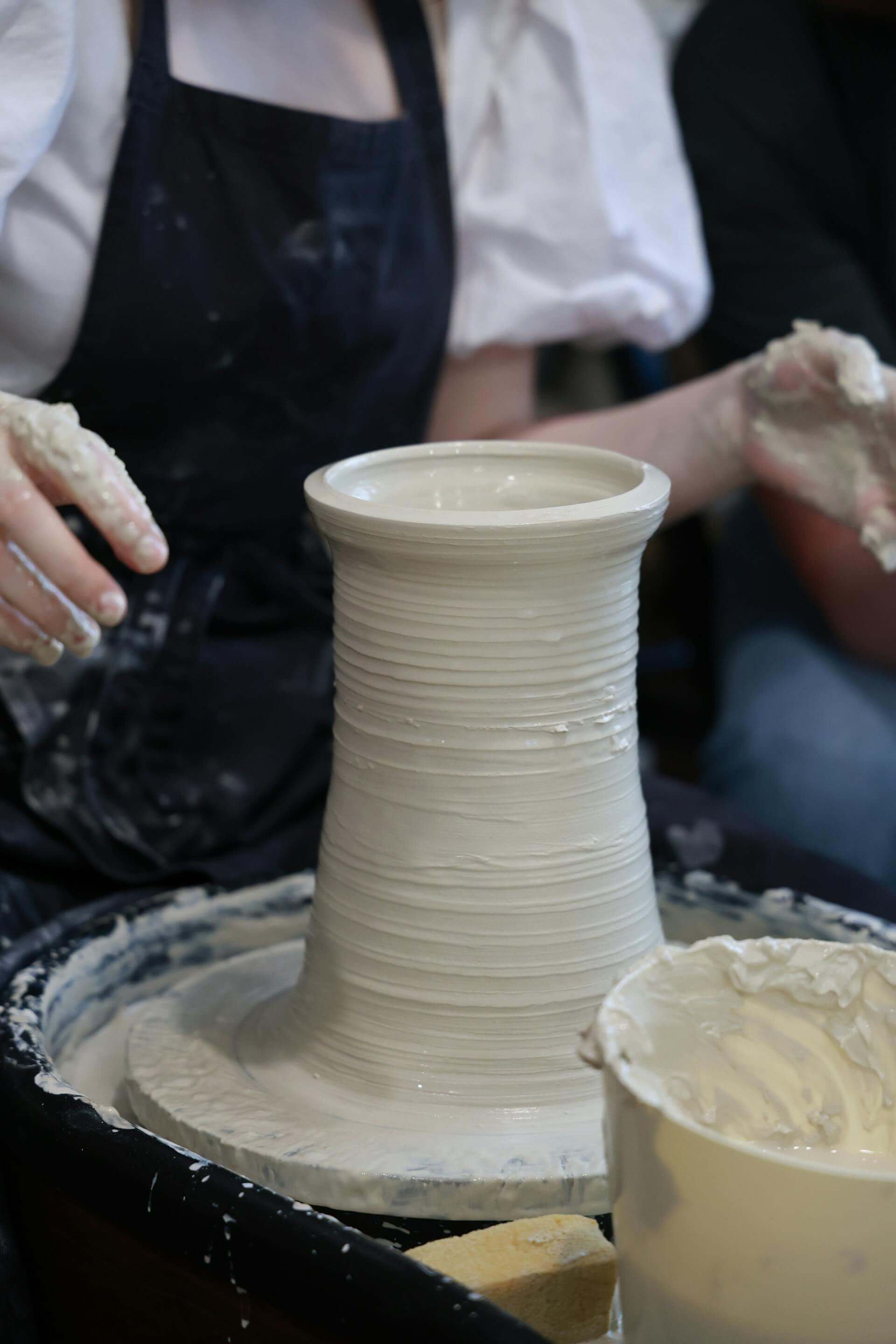 A woman skillfully shapes clay on a potter's wheel, creating a beautiful pot with focused concentration