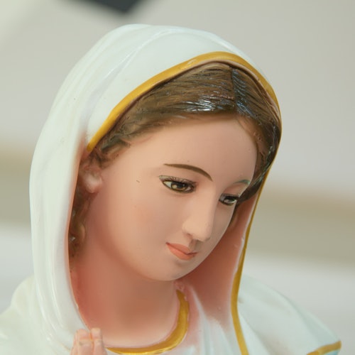 صورة مقربة لتمثال امرأة ترتدي غطاء رأس أبيض وأصفر، بشعر بني فاتح وتعبير هادئ على وجهها.
