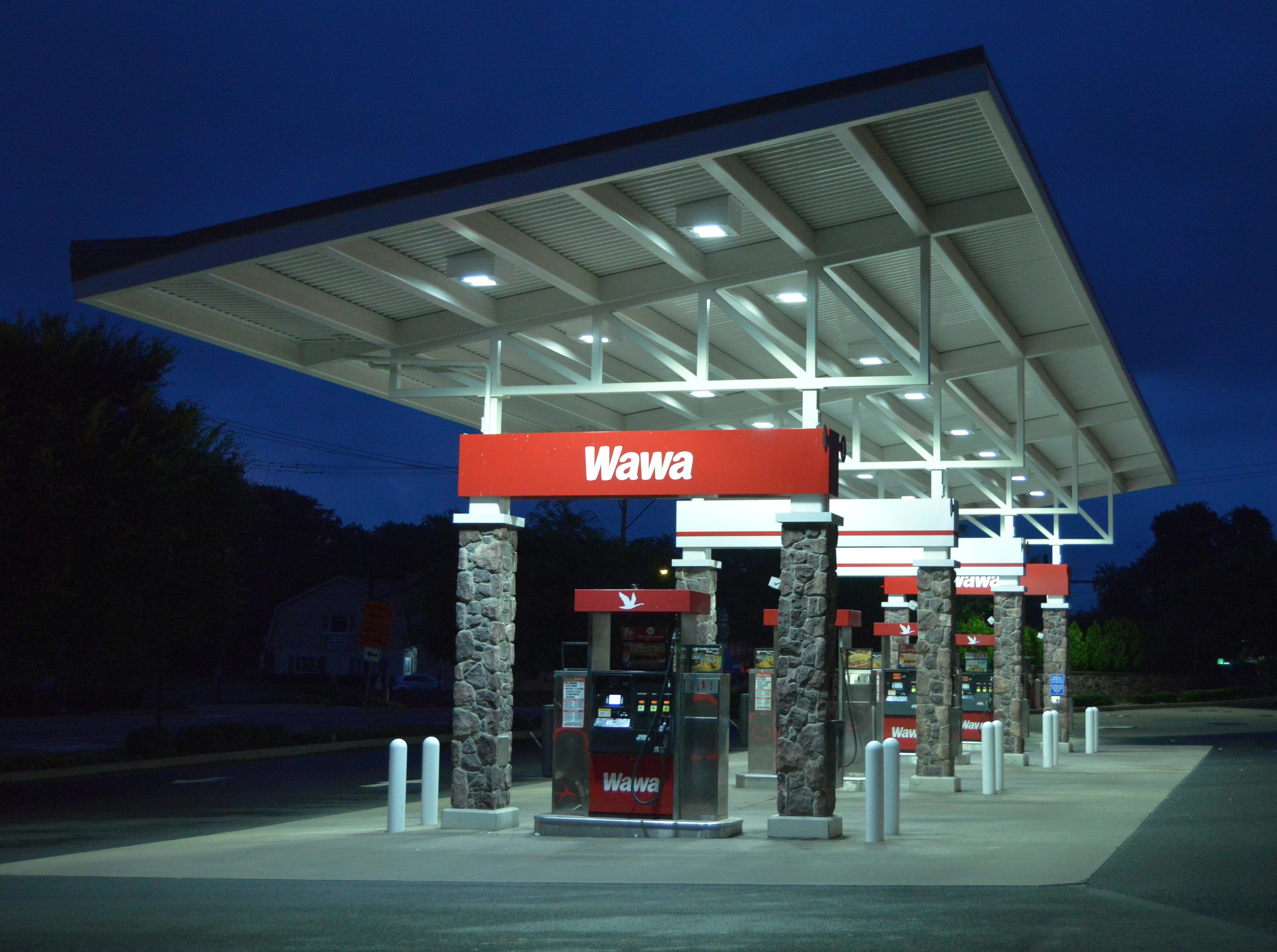 Wawa gas station canopy lit up at night with glowing lights over multiple fuel pumps, creating a clean and well-lit fueling area. Highlights Wawa’s 24-hour convenience for customers.