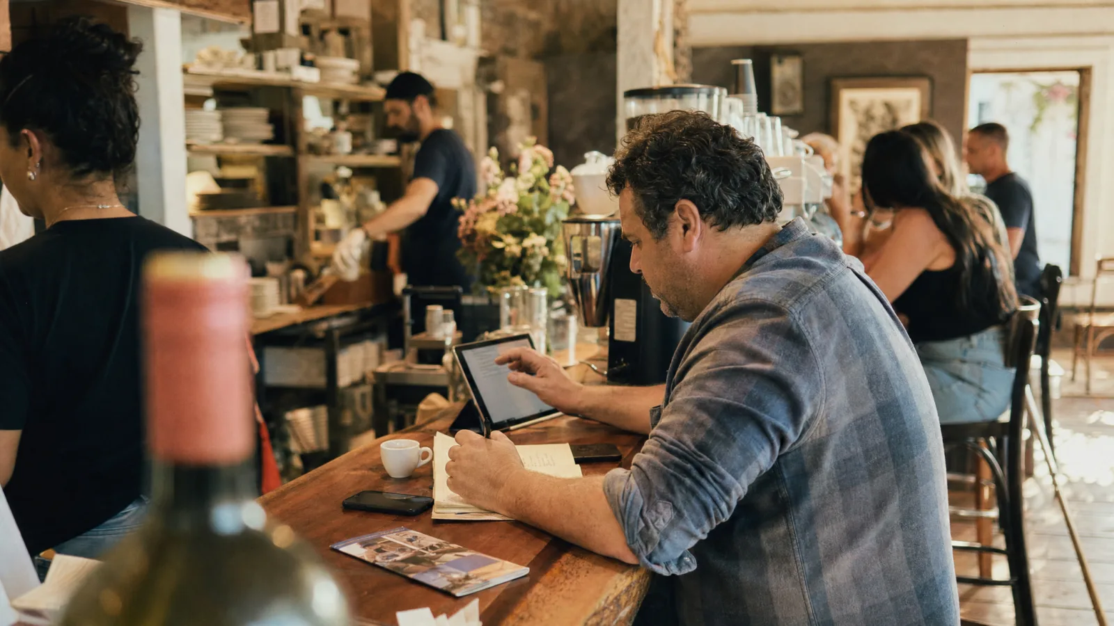 Titolare di bistrot scorre un tablet al bancone e prende appunti accanto a un depliant
