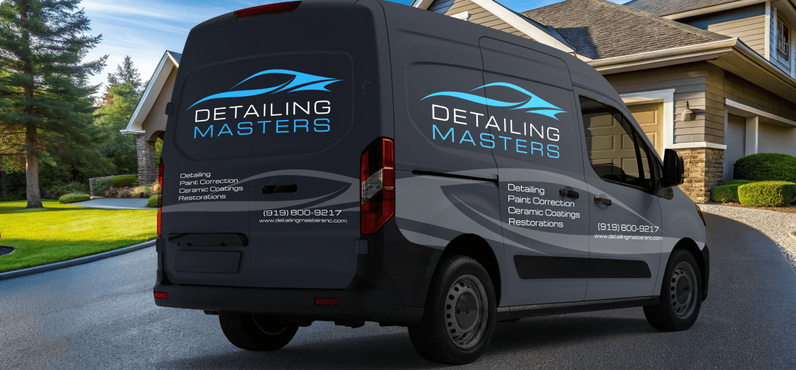 A gray van wrapped in Detailing Masters brand and information parked in the driveway of a luxury home