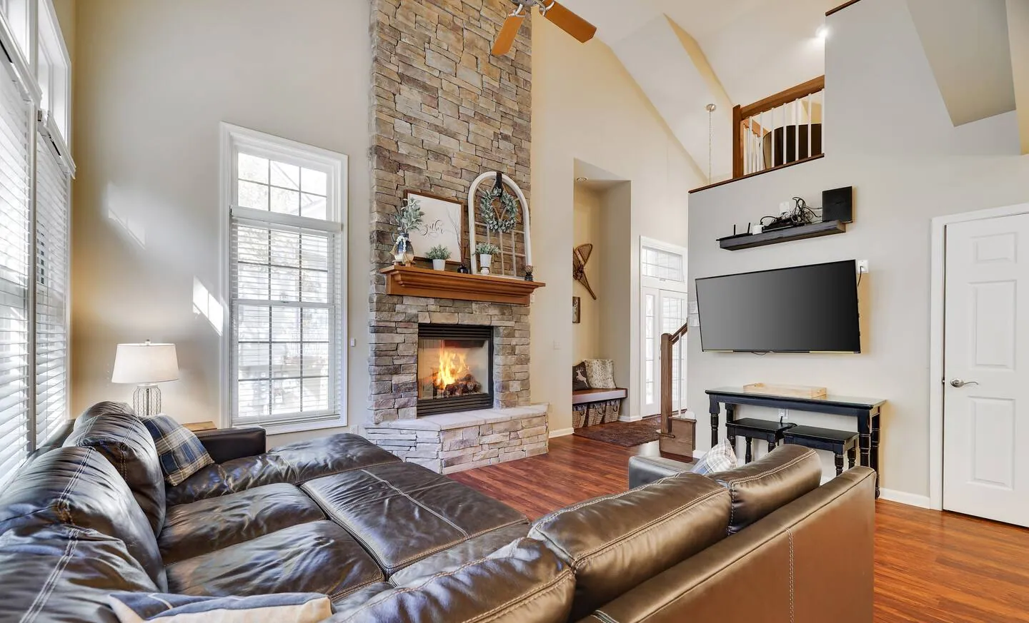 Living room with leather sectional, stone fireplace and tall windows at Mountainwoods Memories