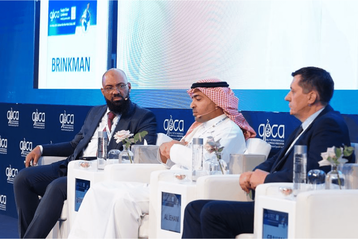 A panel discussion at a professional event, featuring three men, one wearing traditional Middle Eastern attire.