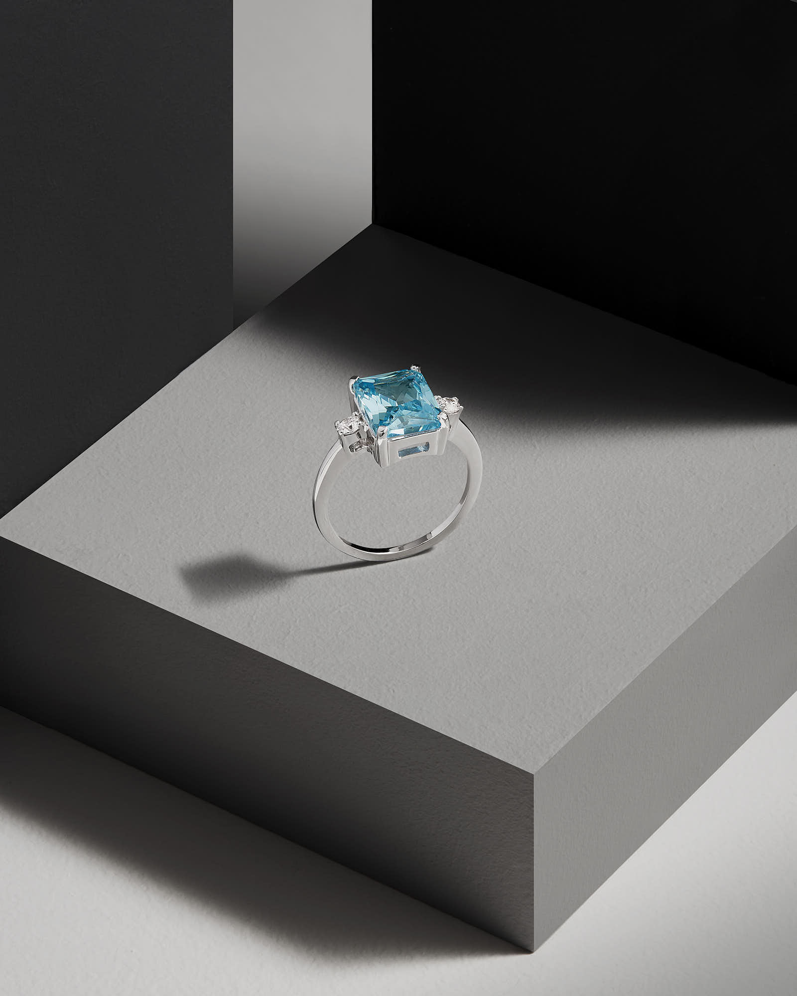 A close-up of a small silver ring with aqua stone on a gray surface, casting a subtle shadow.