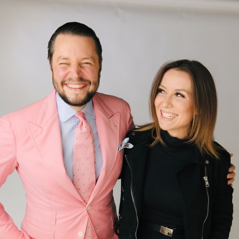 Smiling young man with curly hair, wearing a dark hoodie, against a softly lit background.