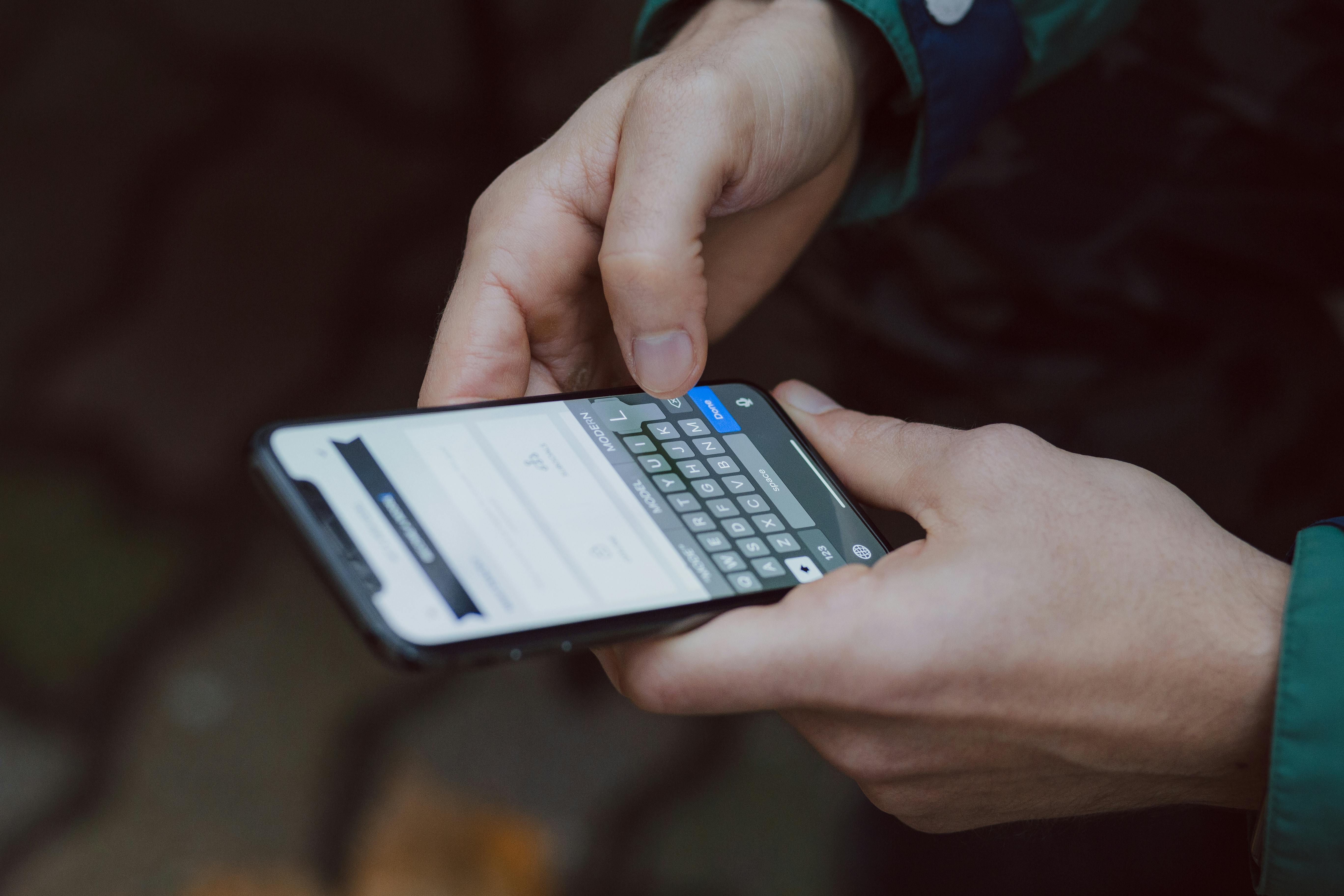 A person holds a smartphone while typing on the screen, with a blurred background.