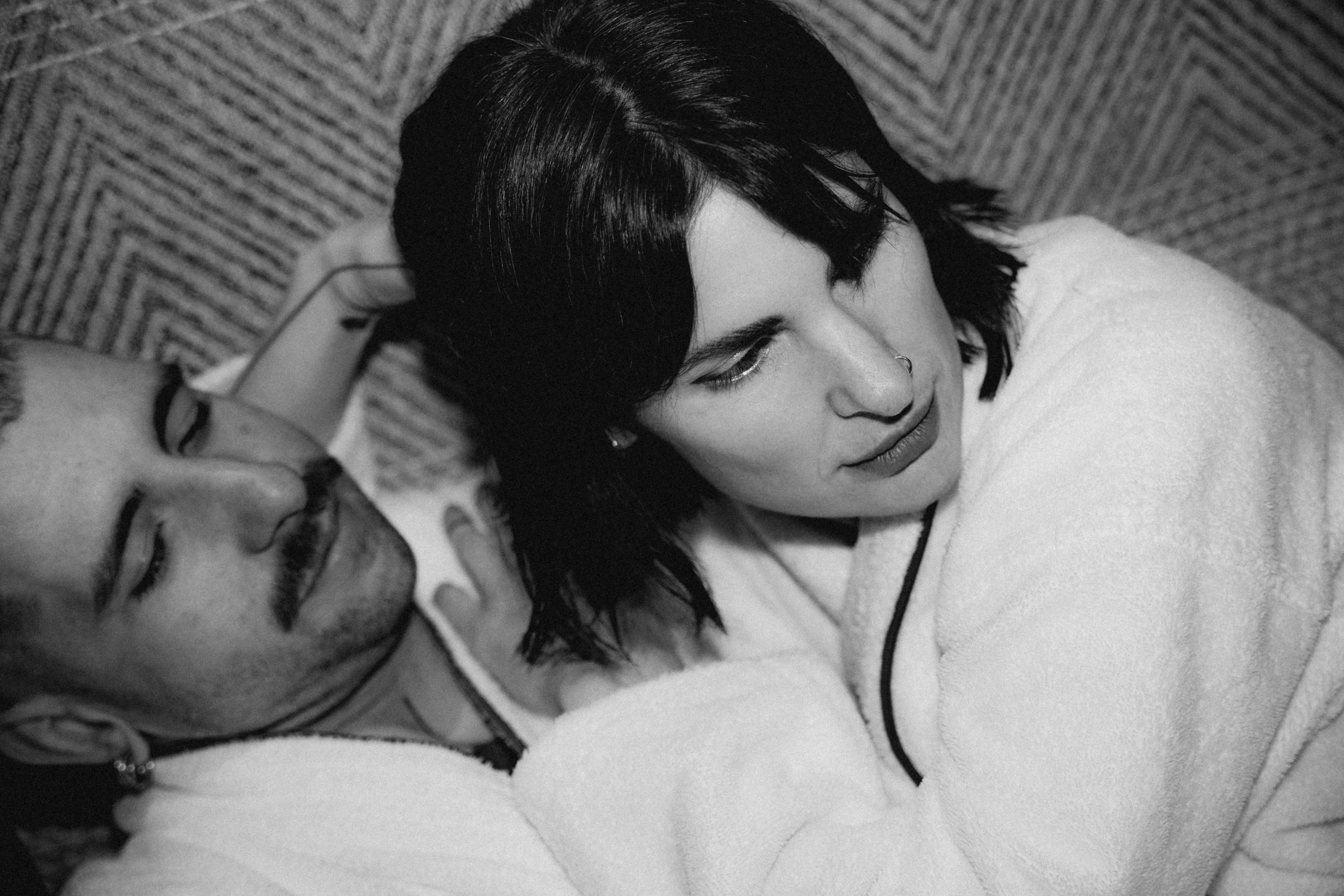 Two people embrace closely, their expressions serene, in a softly lit, intimate setting with a textured background.