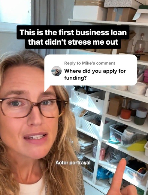 Image of a woman speaking in a home workspace with overlay text saying “This is the first business loan that didn’t stress me out,” alongside a comment asking where she applied for funding, indicating a testimonial-style financial ad.
