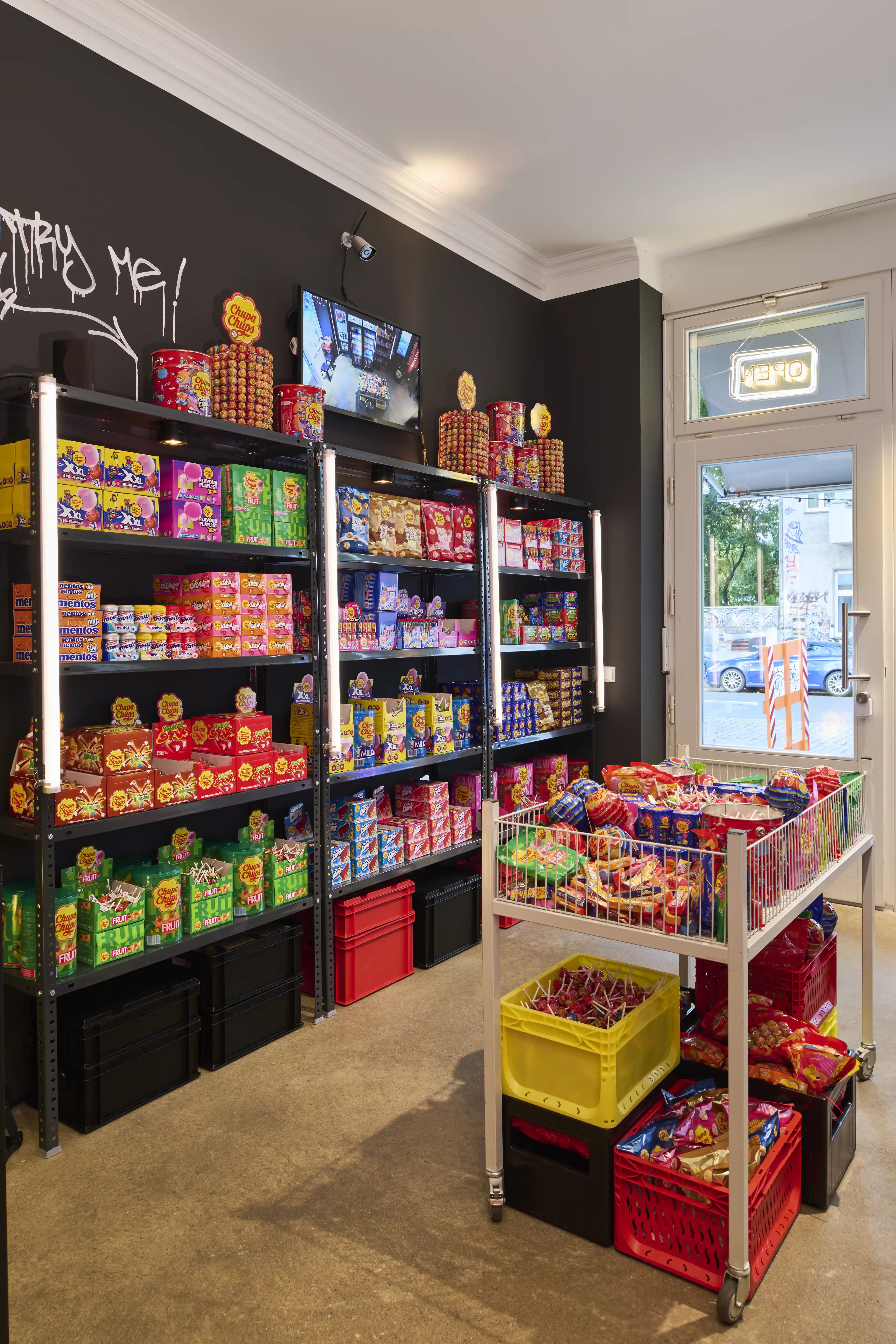 Black shelves stocked with colorful candy boxes and red crates inside the Chupa Chups pop-up kiosk.
