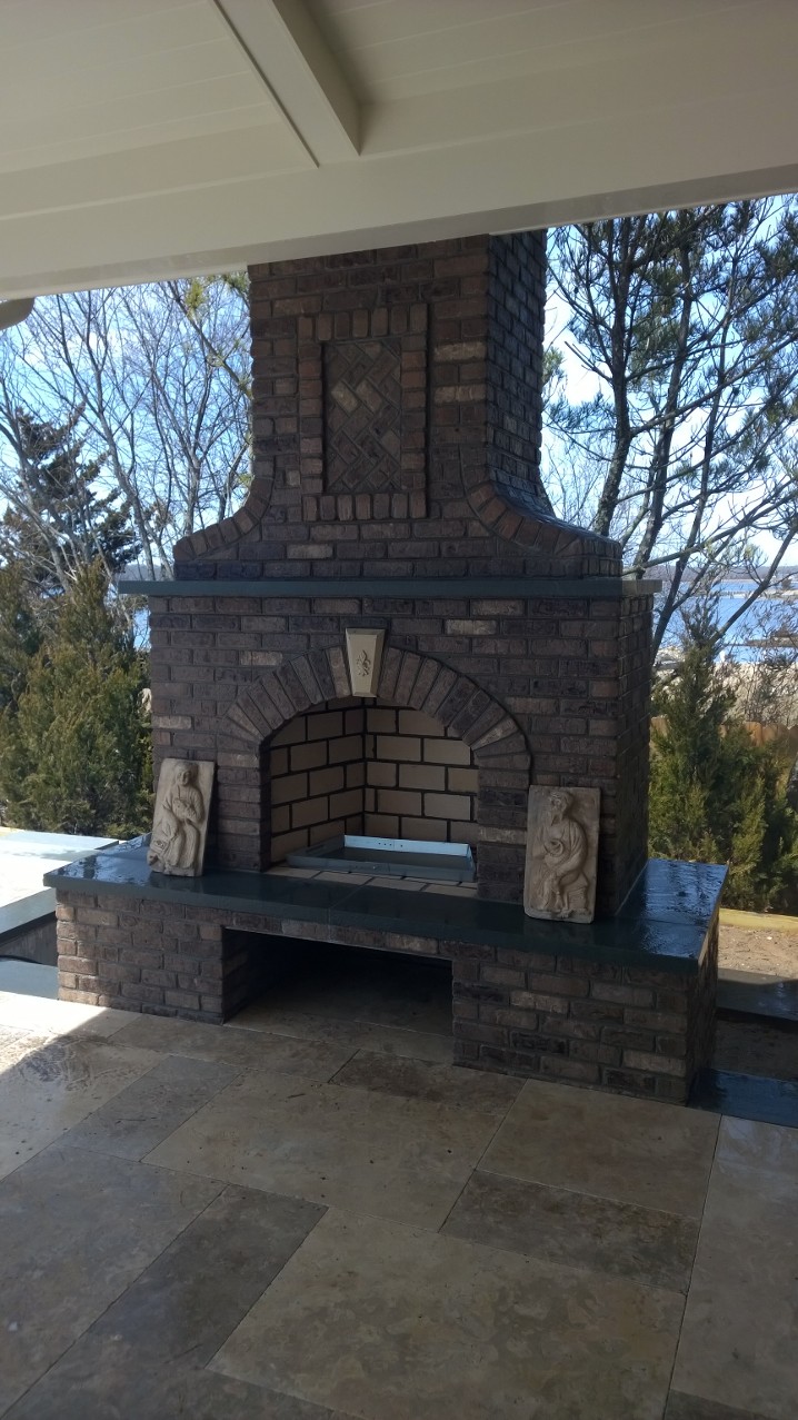 White dome pizza oven on stone base with fish accent and wood storage