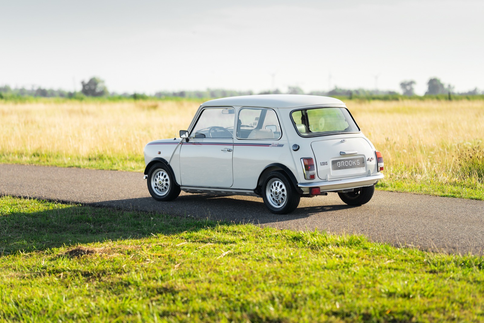 A classic white car parked on a road, surrounded by lush green fields under a clear blue sky.