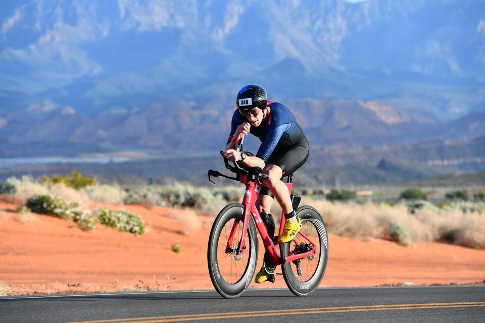 Triathlete in a blue tri suit riding a red tri bike through the Utah desert