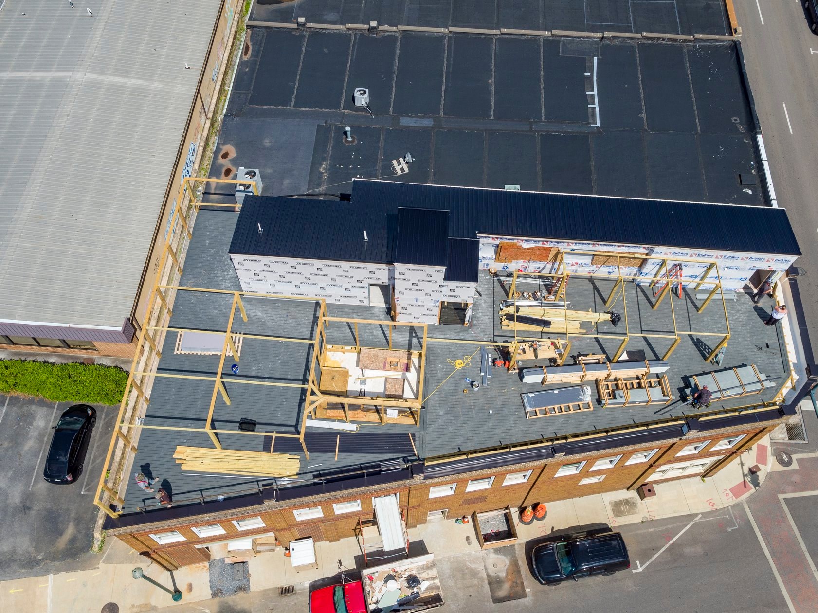 Aerial view of a building complex with construction materials and vehicles parked in a lot nearby.