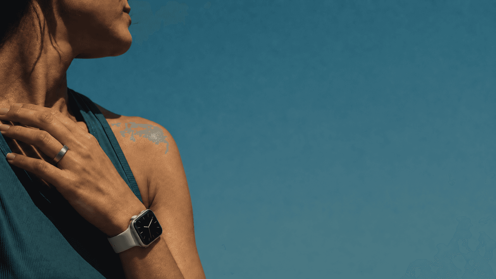 Woman wearing a silver smart ring and ivory-band watch in cinematic shadow against a teal background