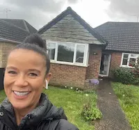 Woman with short hair smiling in front of a brick house with a bay window