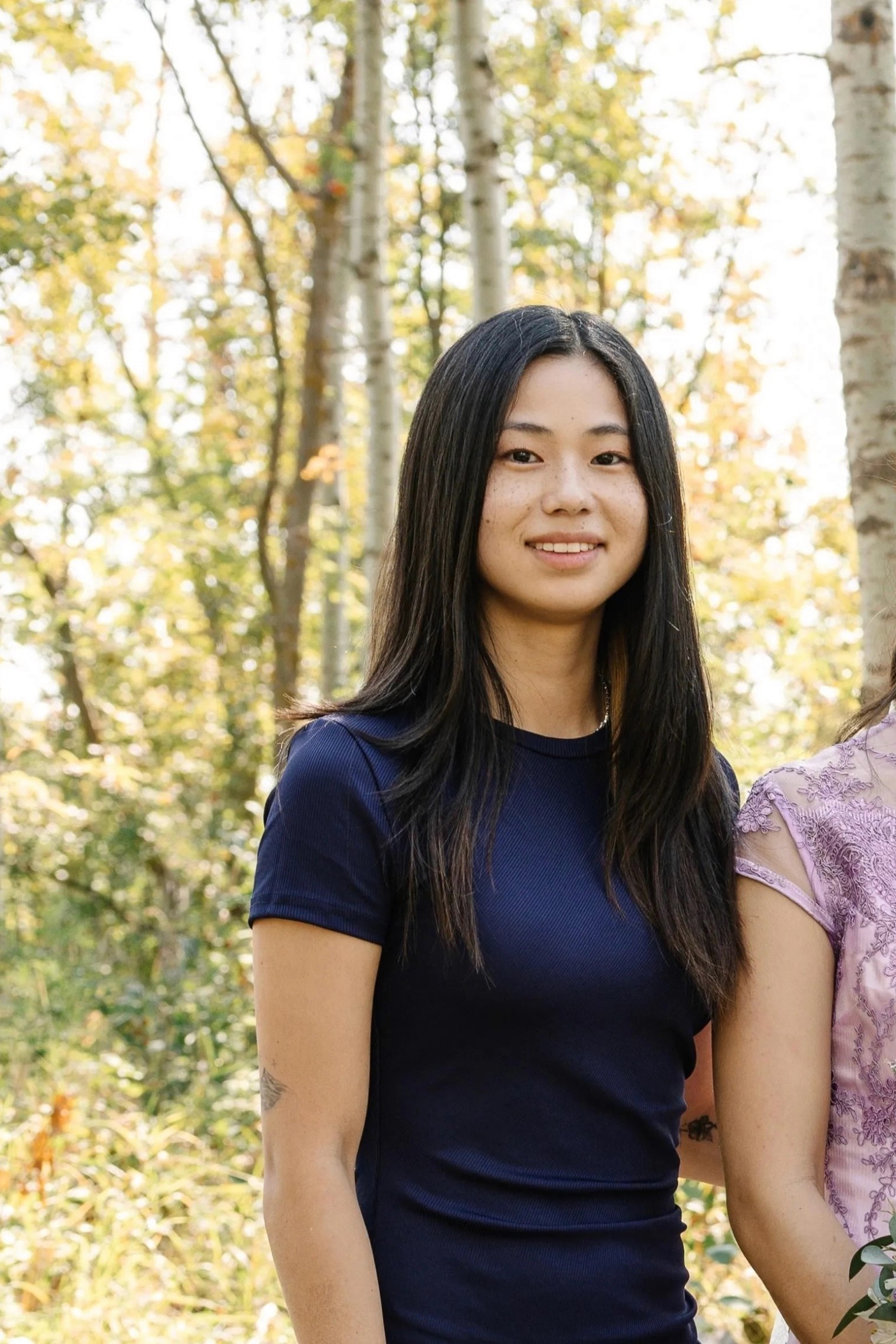 A smiling couple sits on a white blanket in a lush green field.