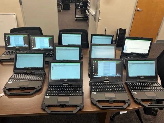 Two individuals working at computer stations, with code displayed on large monitors—representing cybersecurity operations or secure software development in progress.