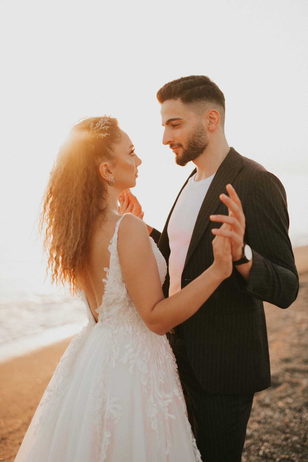 Bride and groom dancing close on a beach with the setting sun behind them