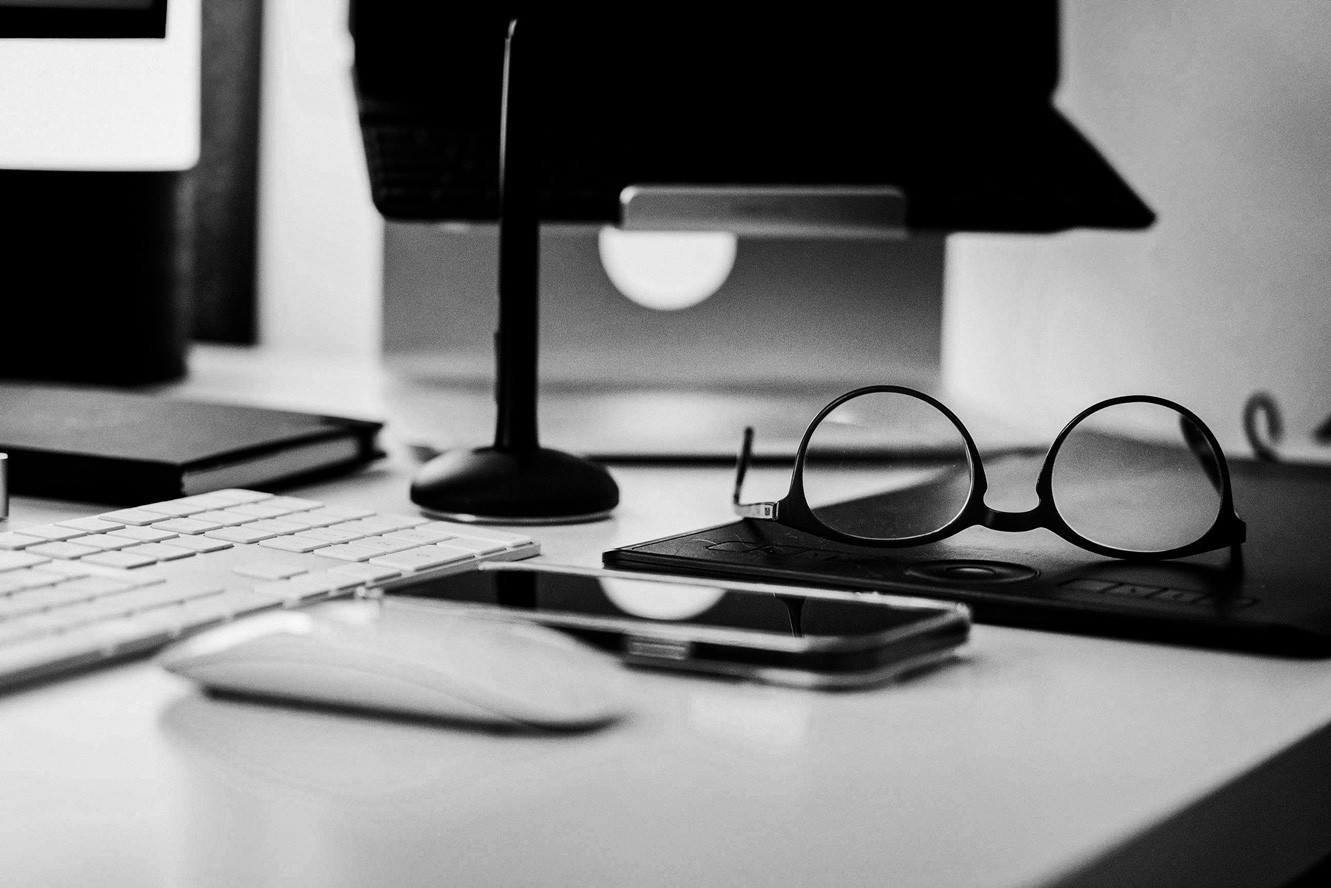 Bureau professionnel avec clavier, smartphone, lunettes et écran d'ordinateur, environnement de travail digital en noir et blanc