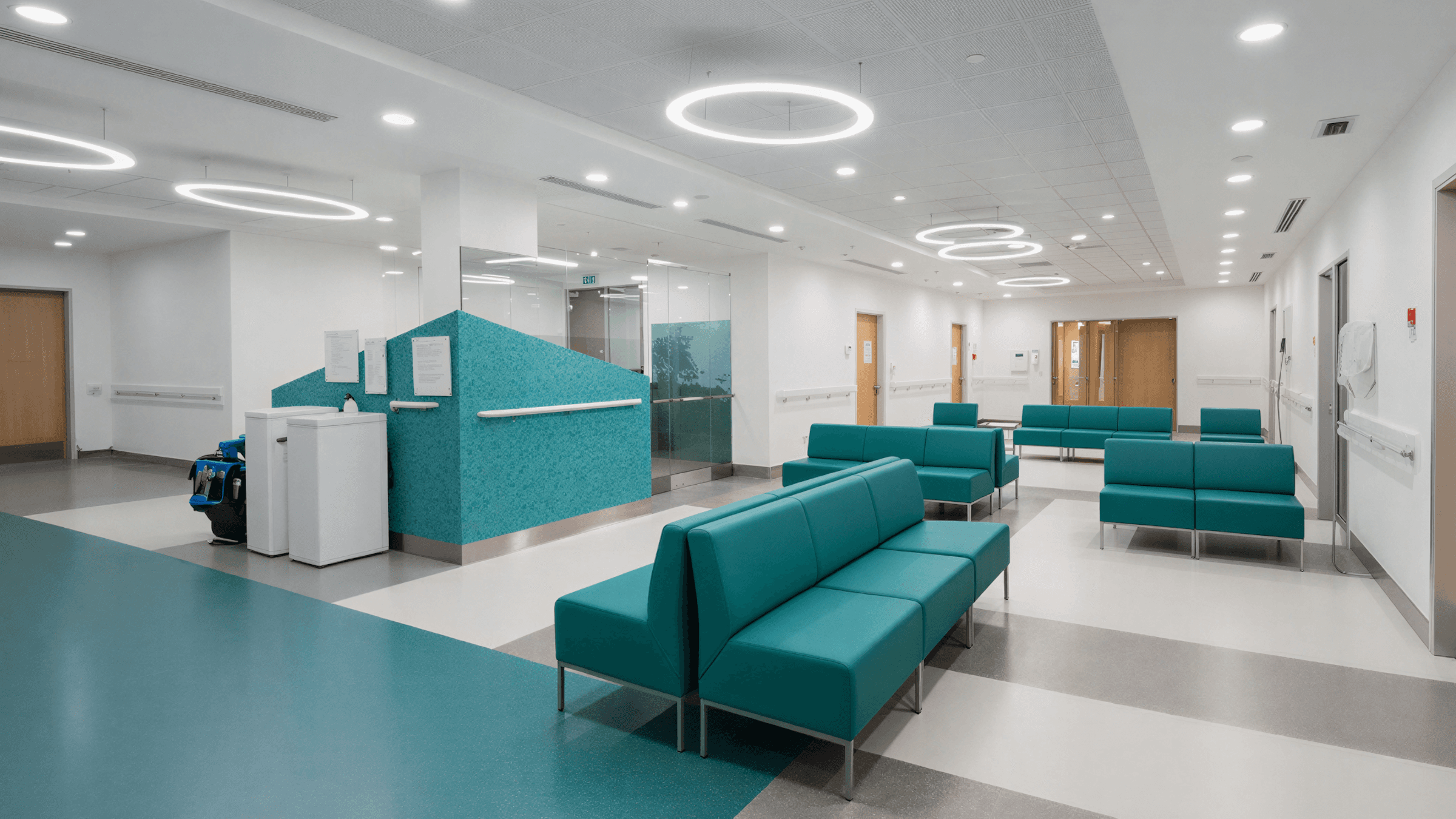 Modern hospital interior featuring teal seating and bright, spacious layout. Clear, clean, and well-lit environment.