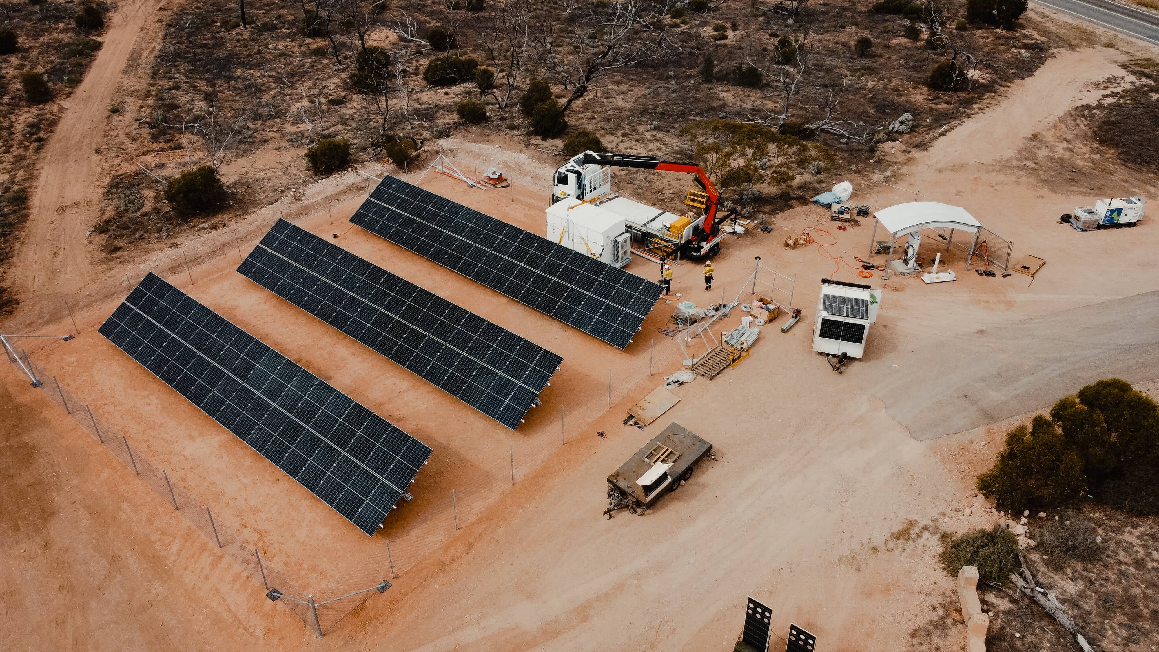 Aerial view of a remote solar power installation site with multiple solar panels, a crane truck, and equipment, Powerhouse Renewables Group.