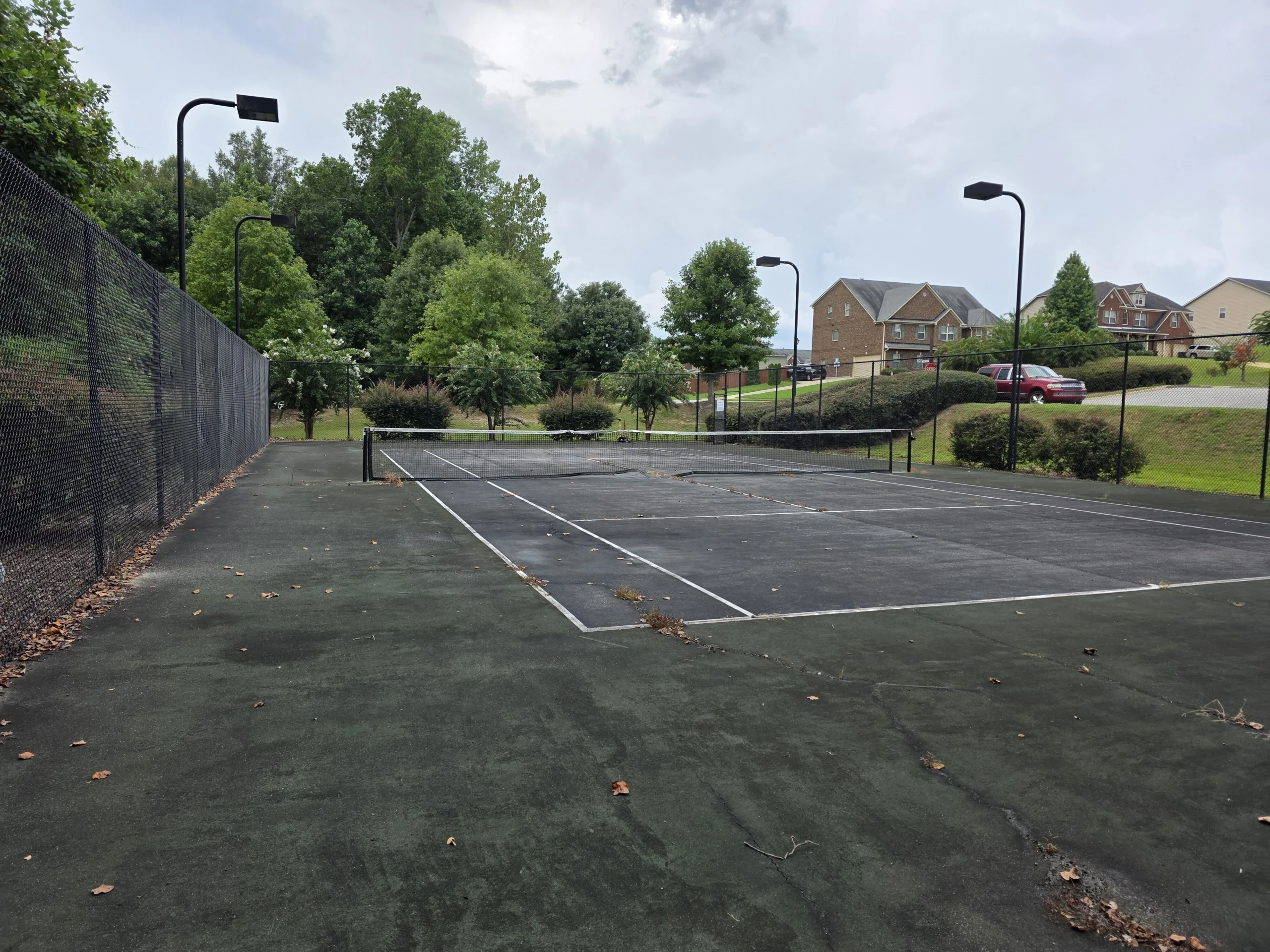Worn tennis court before resurfacing showing cracked asphalt and faded green out-of-bounds in Fort Mitchell, AL