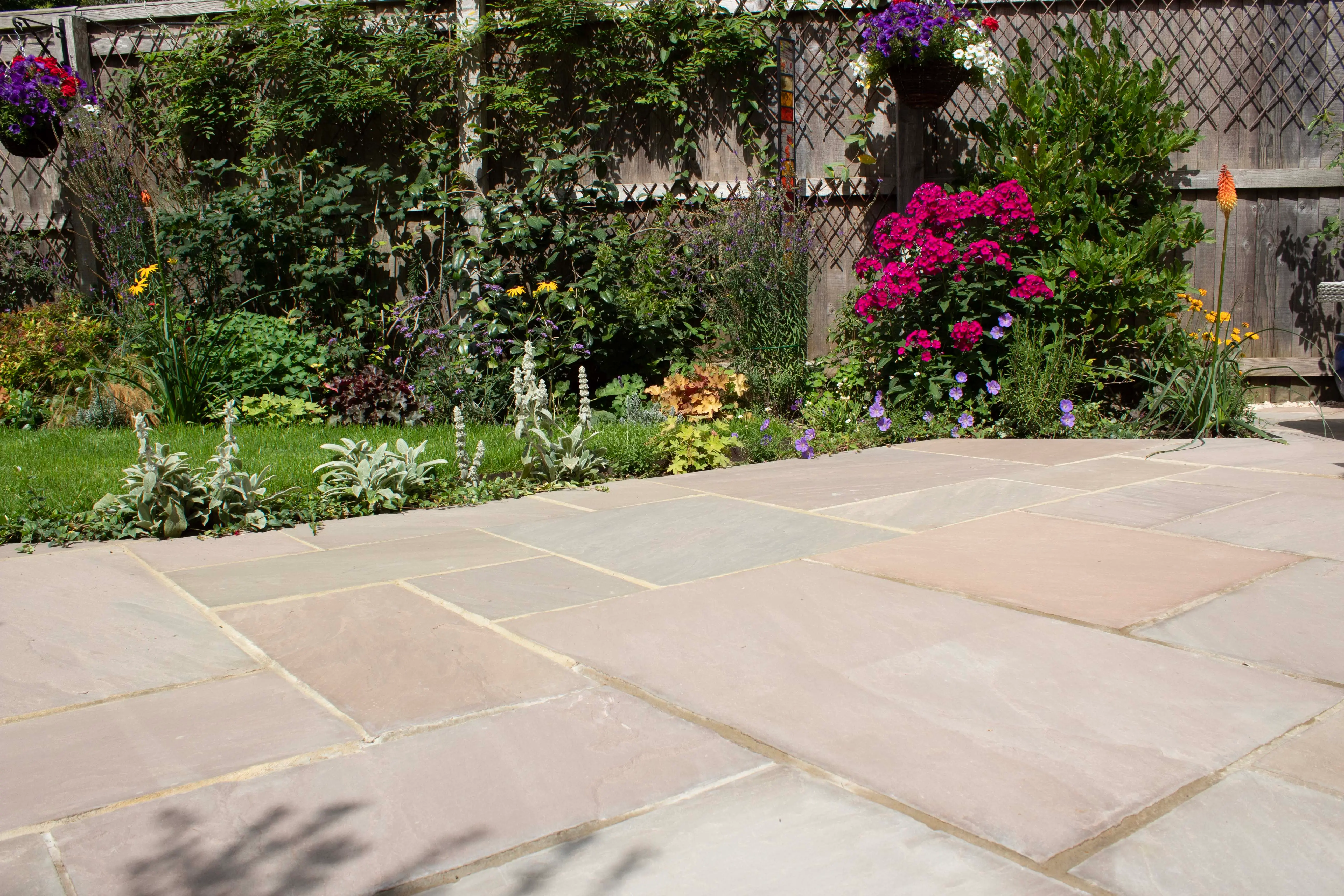 A sunny garden scene with colorful flowers and greenery, featuring a stone pathway.