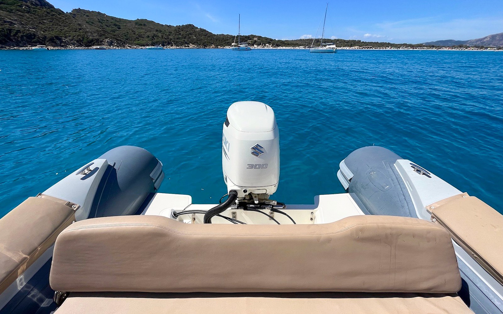 Boat deck view on the Gulf of Cagliari with distant sailboats and coastline.