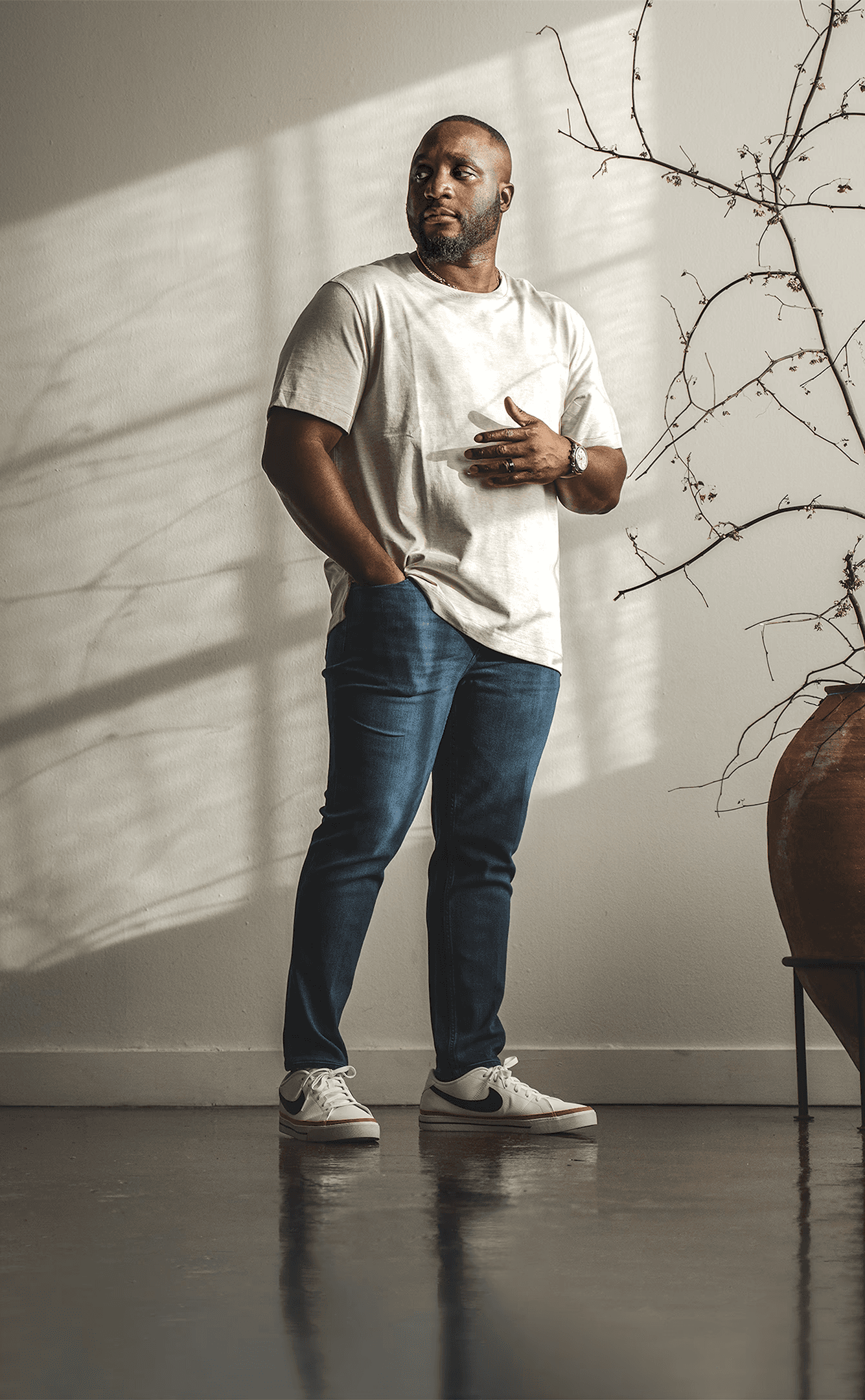 Tade Bolarin, executive and life coach for ambitious professionals, standing in a Japandi minimalist loft, wearing casual beige t-shirt, blue jeans, and Nike shoes.