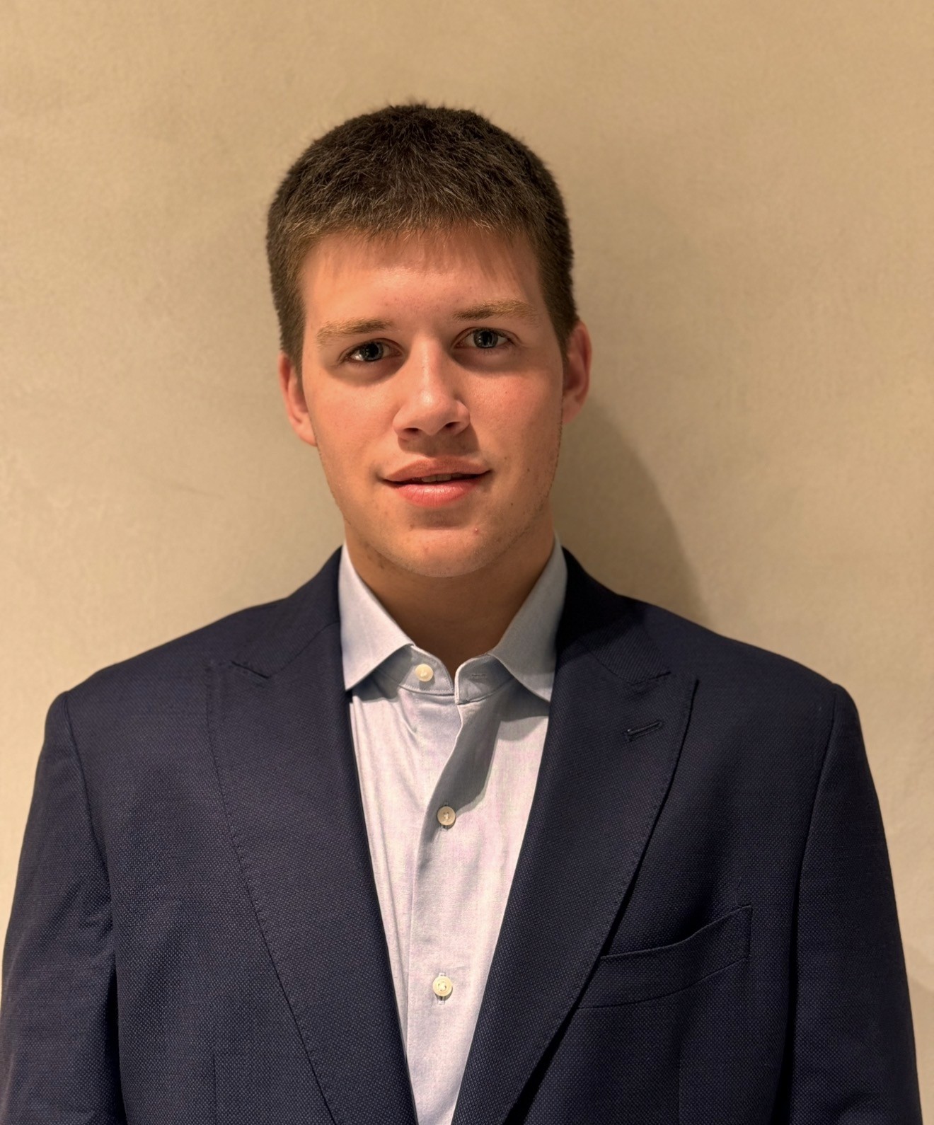 A focused woman with long red hair is seated at a desk, wearing a black blazer and dark blouse. She intently looks at camera, smiling slightly, with an open laptop in front of her. The setting is a warm and serene office setup in the background. Soft daylight filters through, creating a calm atmosphere. The composition captures her in a frontal profile with a clear emphasis on her concentration and the serene indoor setting.