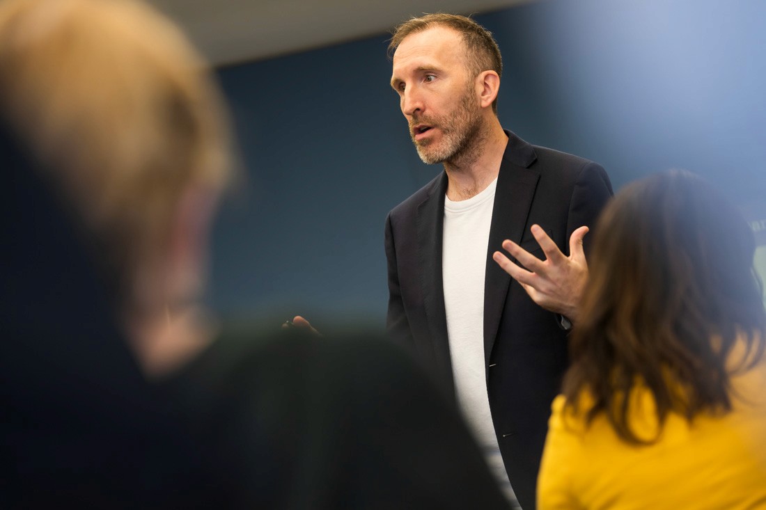 A 3D character viewed from behind with pastel pink hair styled in two buns, wearing a blue knitted sweater and hoop earrings on a light gray background.