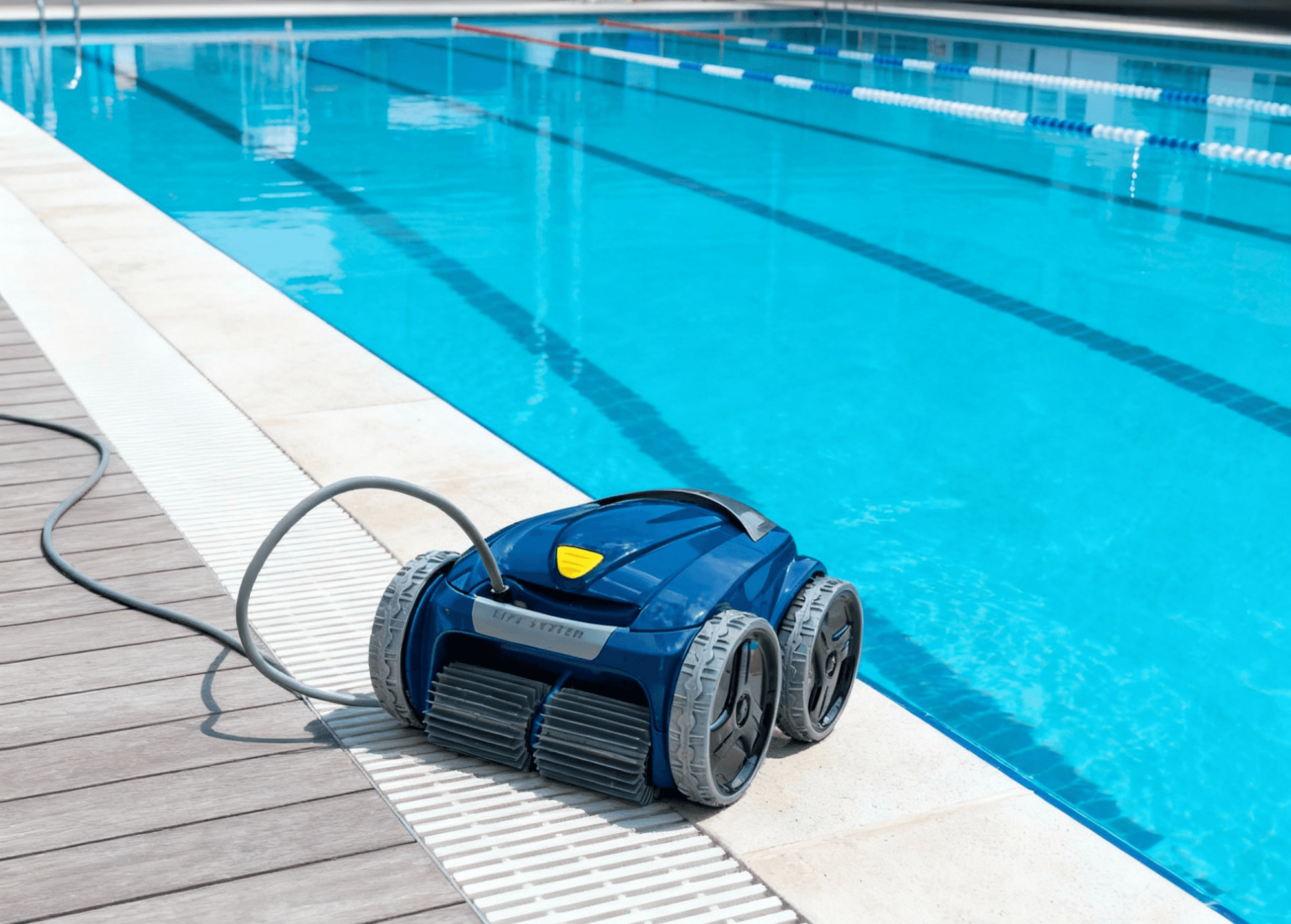 Robotic pool cleaner positioned beside a bright blue lap pool on a sunny day.