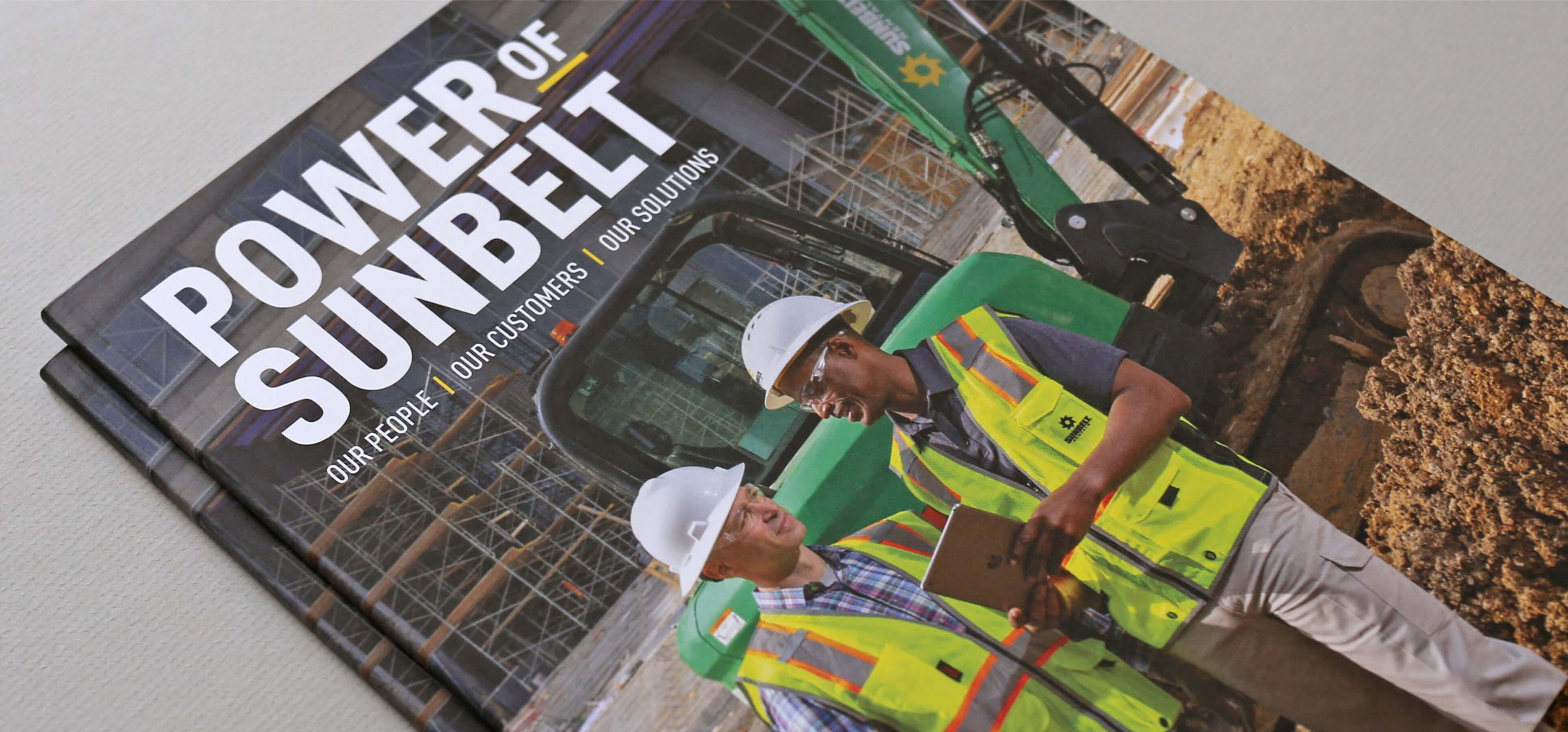 Front cover of the Sunbelt Publication featuring two employees in safety gear at a construction site, standing near a Sunbelt-branded bulldozer.