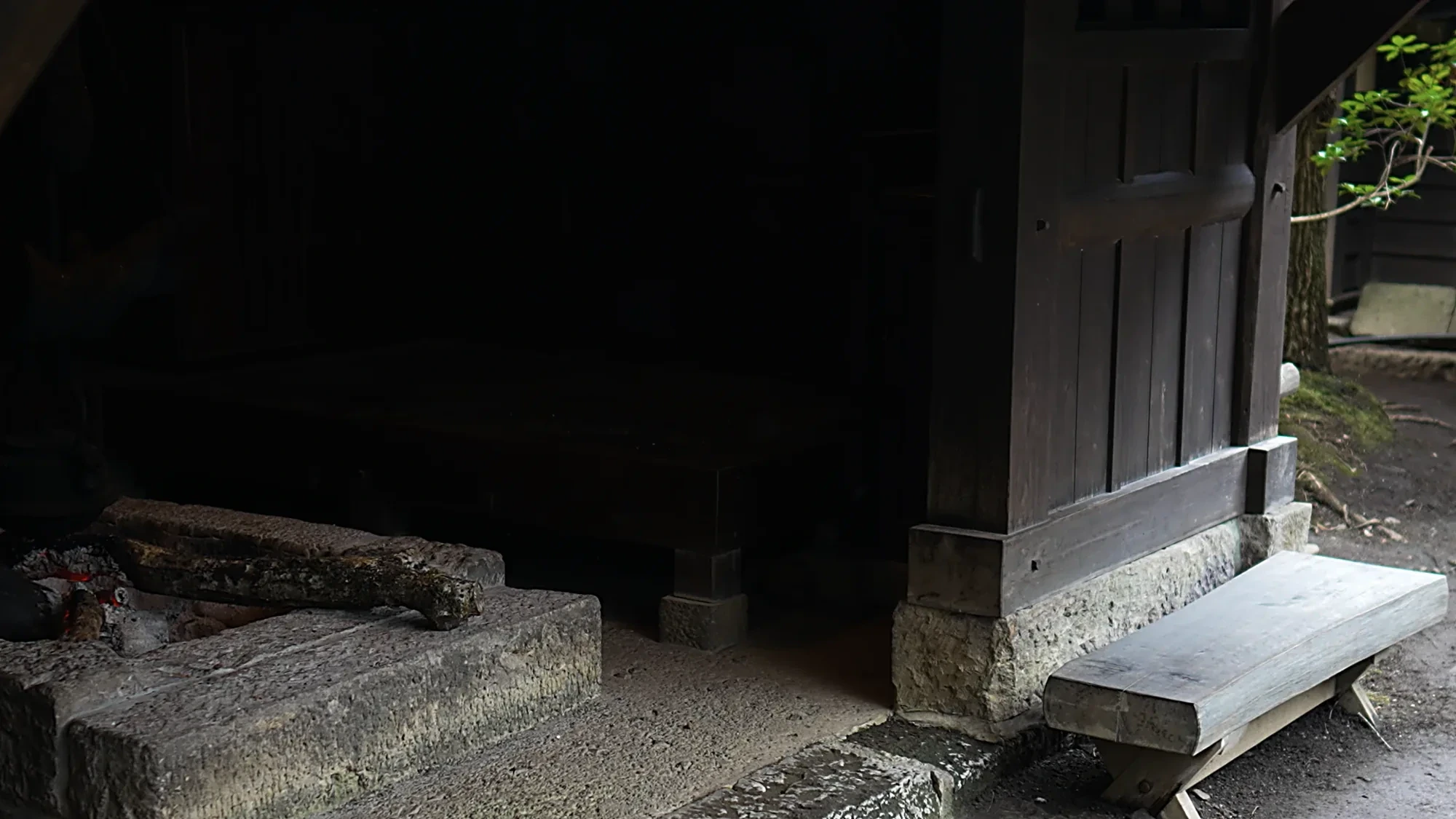 A dark timber inn entrance at Kurokawa Onsen with a stone trough and a timber bench