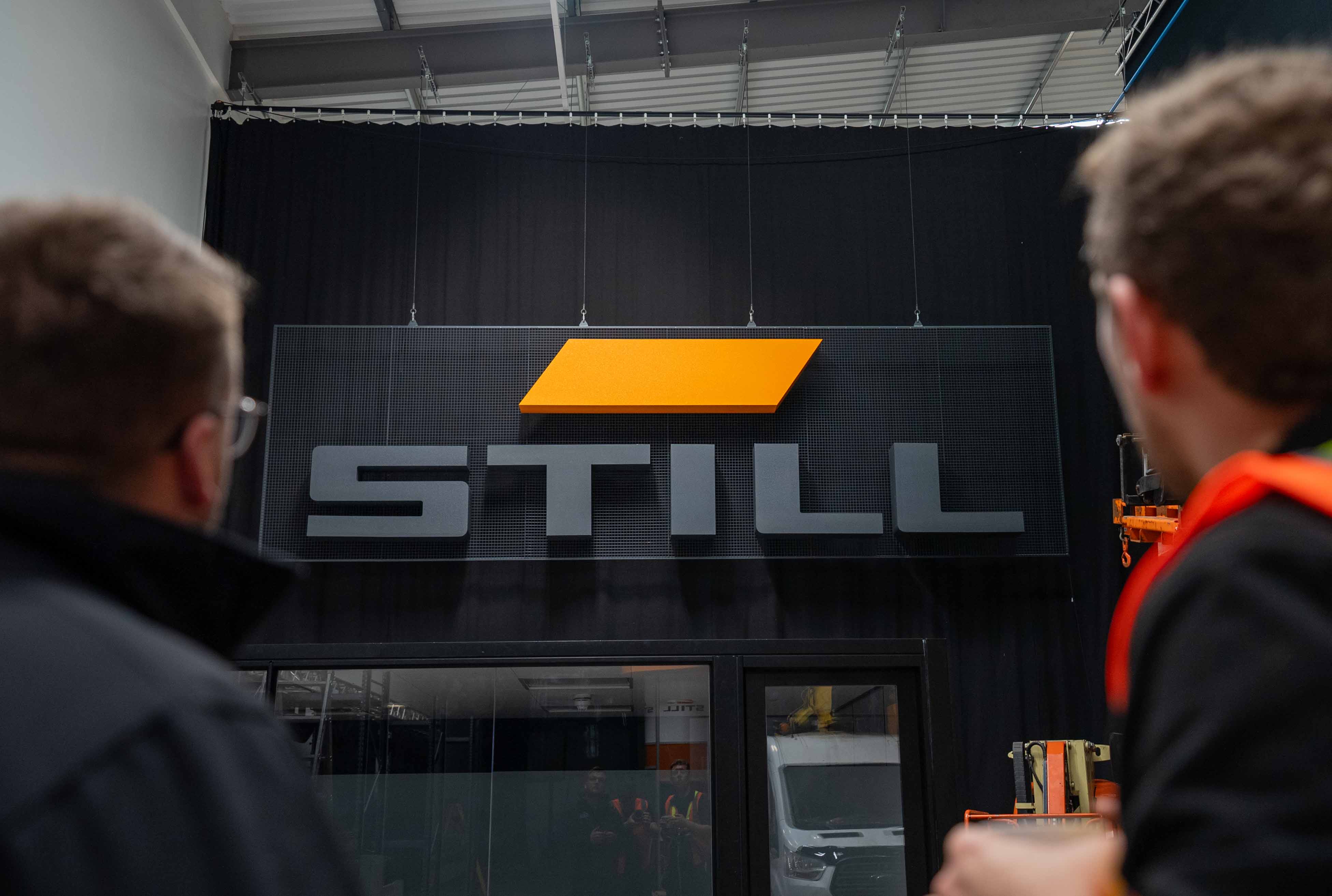 Large STILL branded signage installation with suspended scenic panels and black drape in an event production warehouse.