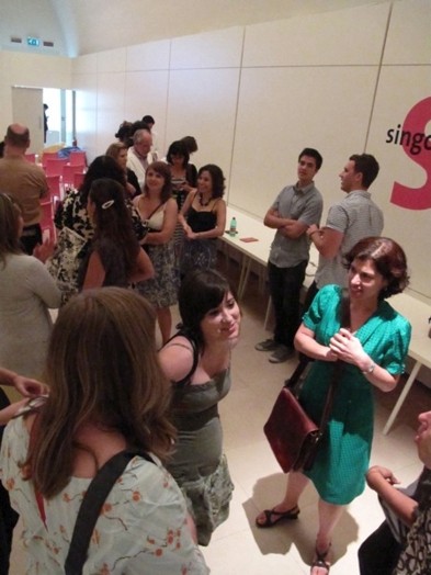 A photo of a group of persons siting in a hall room and talking.