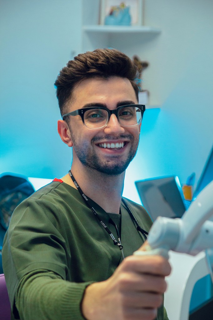 Smiling man wearing glasses and a pink shirt, showing his arm with a bandage after vaccination.