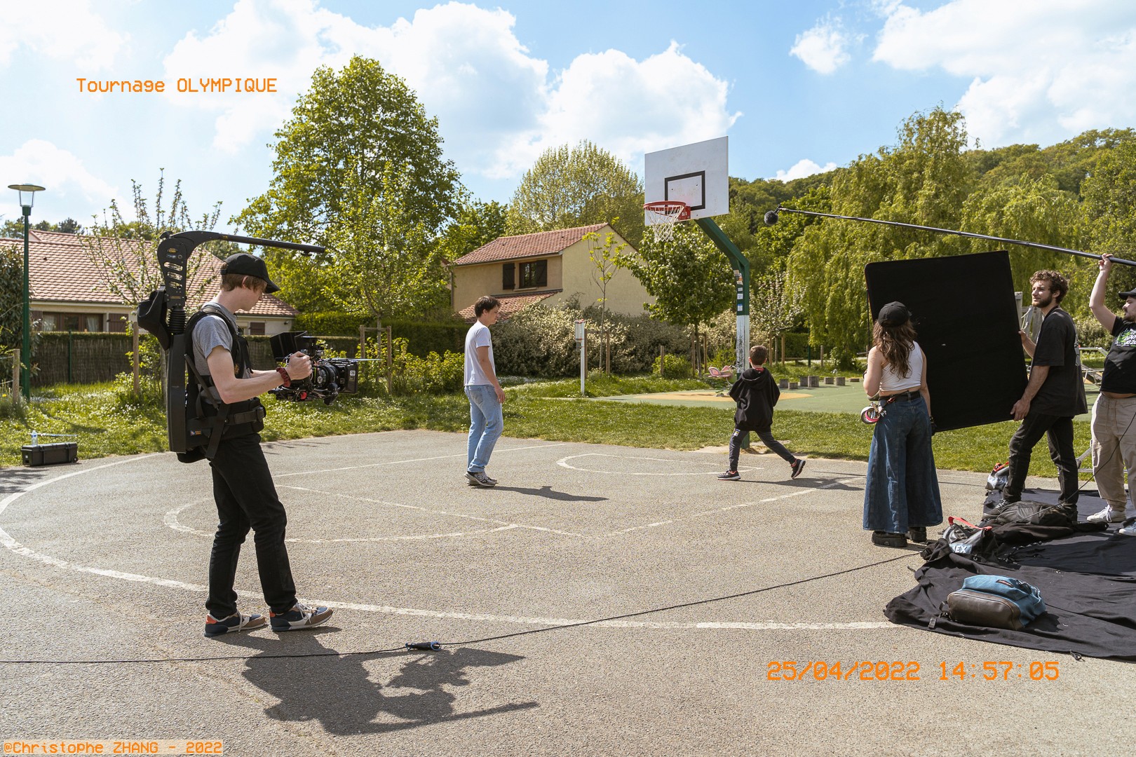 Tournage sur un terrain de basket, avec caméraman et acteurs en action.