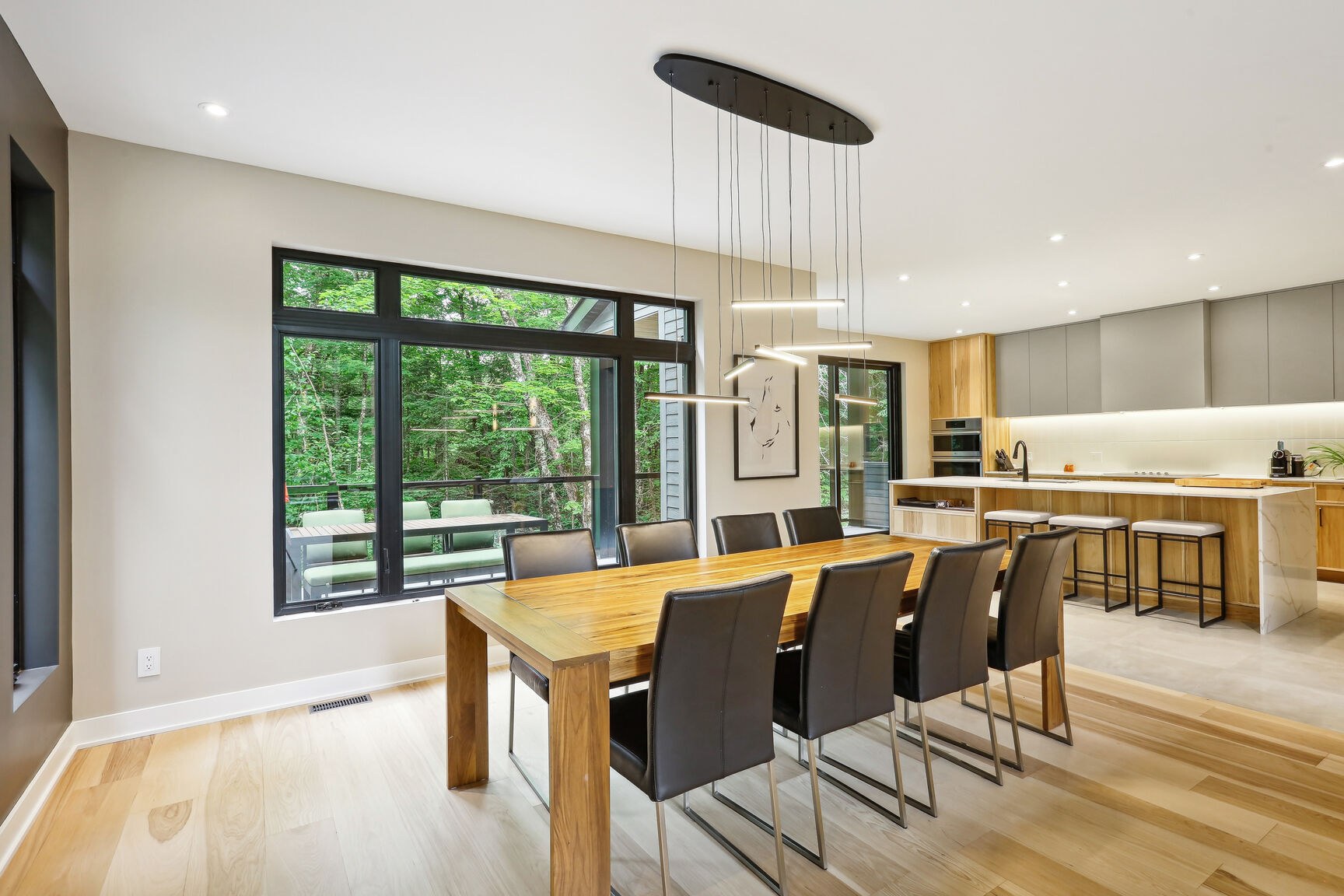 Vue salle à manger vers la cuisine, grandes baies donnant sur le boisé.