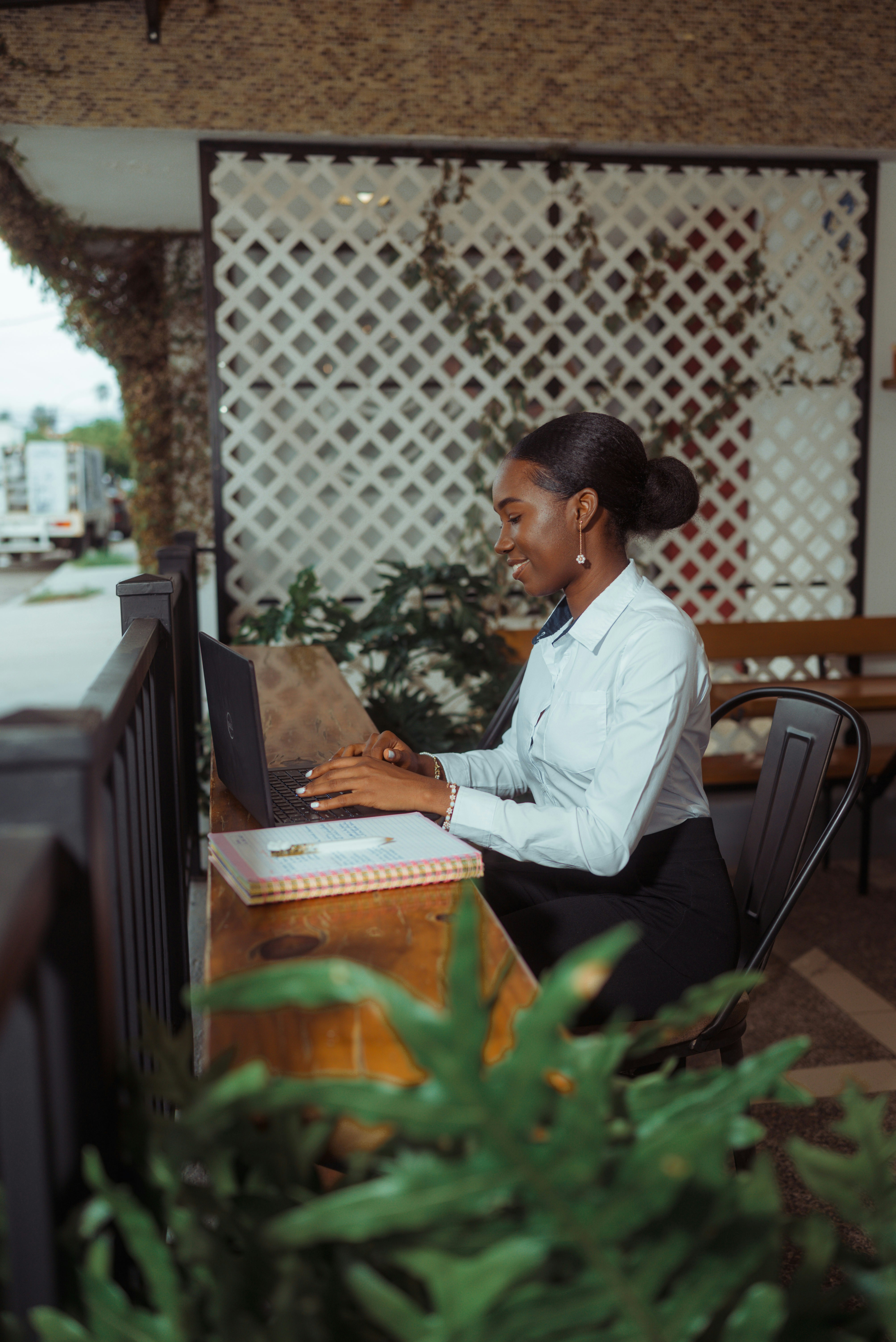 A woman smiling while working on a laptop outdoors.